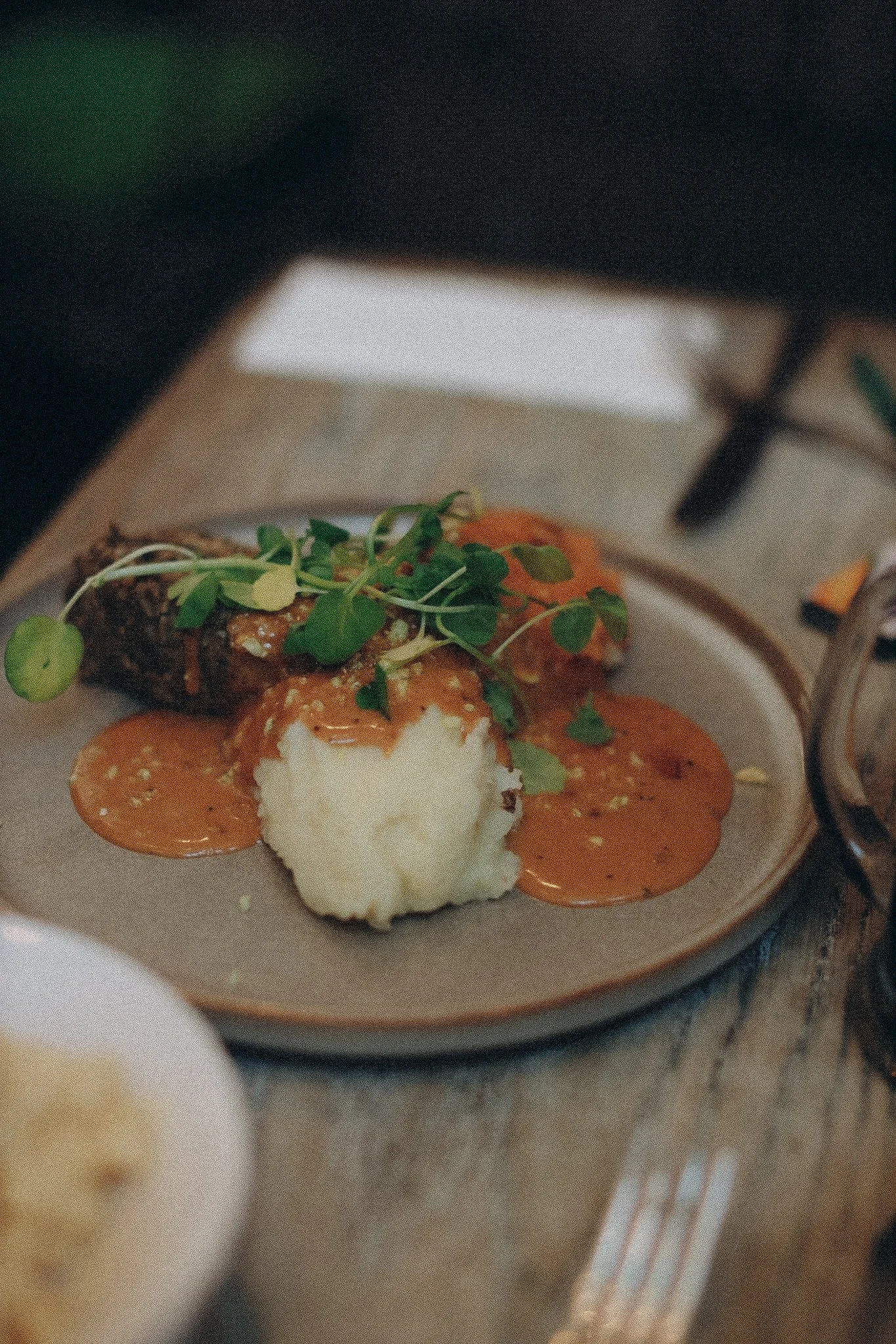 A plate of meatloaf with mashed potatoes, gravy, and microgreens, on a wooden table.
