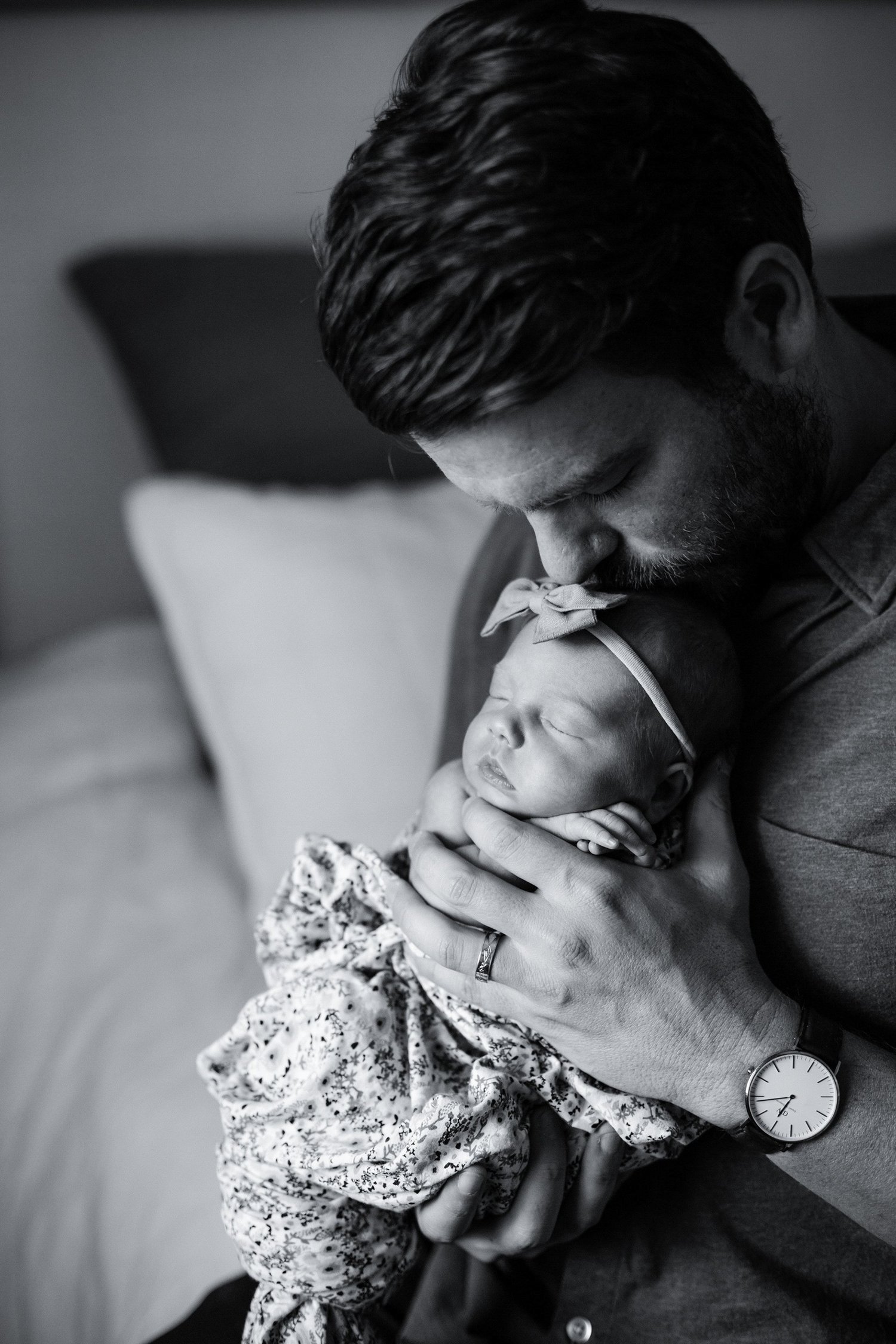 A man holding a newborn baby close to his face in an intimate moment, both appearing peaceful and content, in black and white.