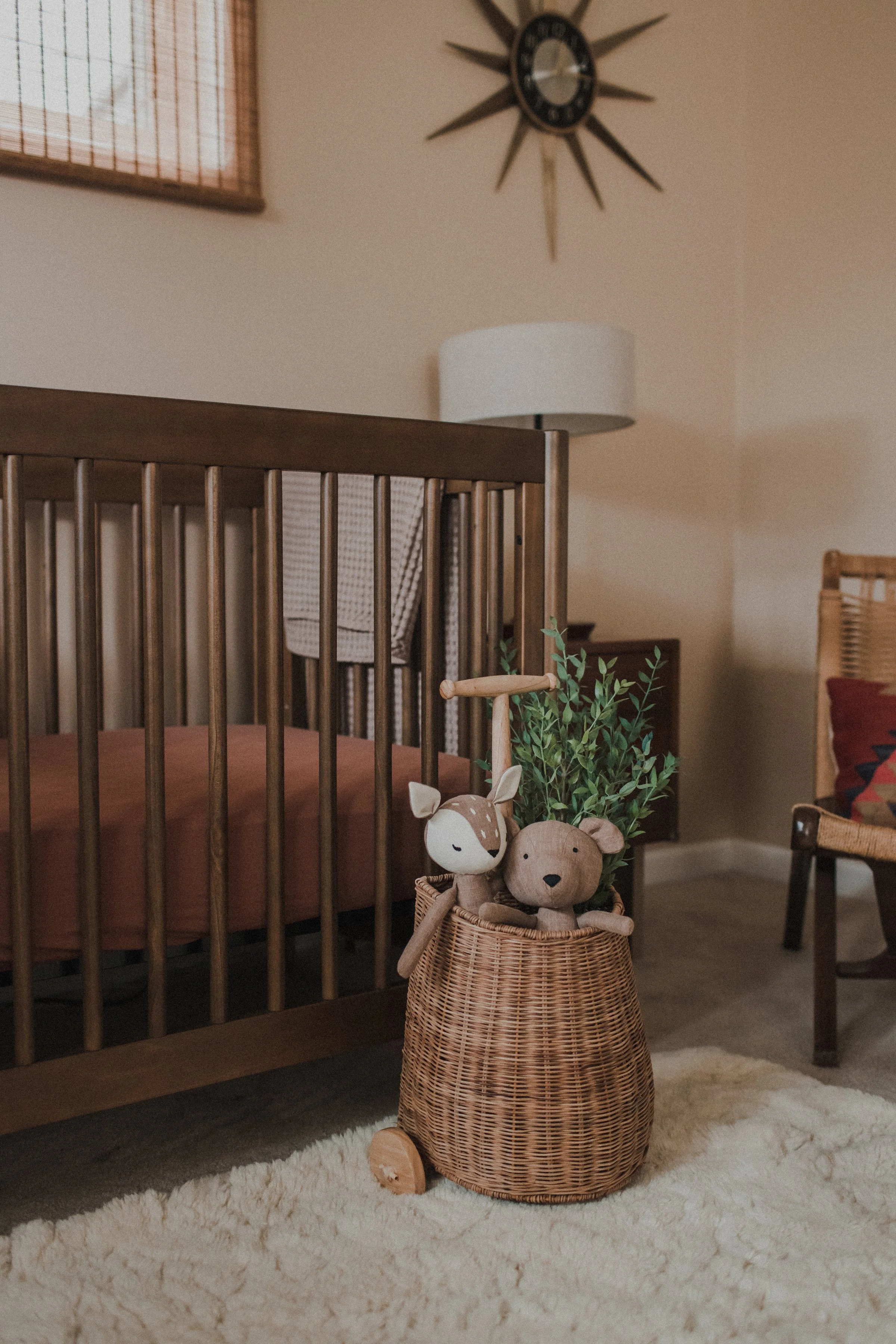 A wicker storage basket with wooden wheels holds plush animal toys, including a deer and a bear, and a small green plant in a cozy, warmly lit room with mid-century decor. Product Photography Shoot Evanston, IL.