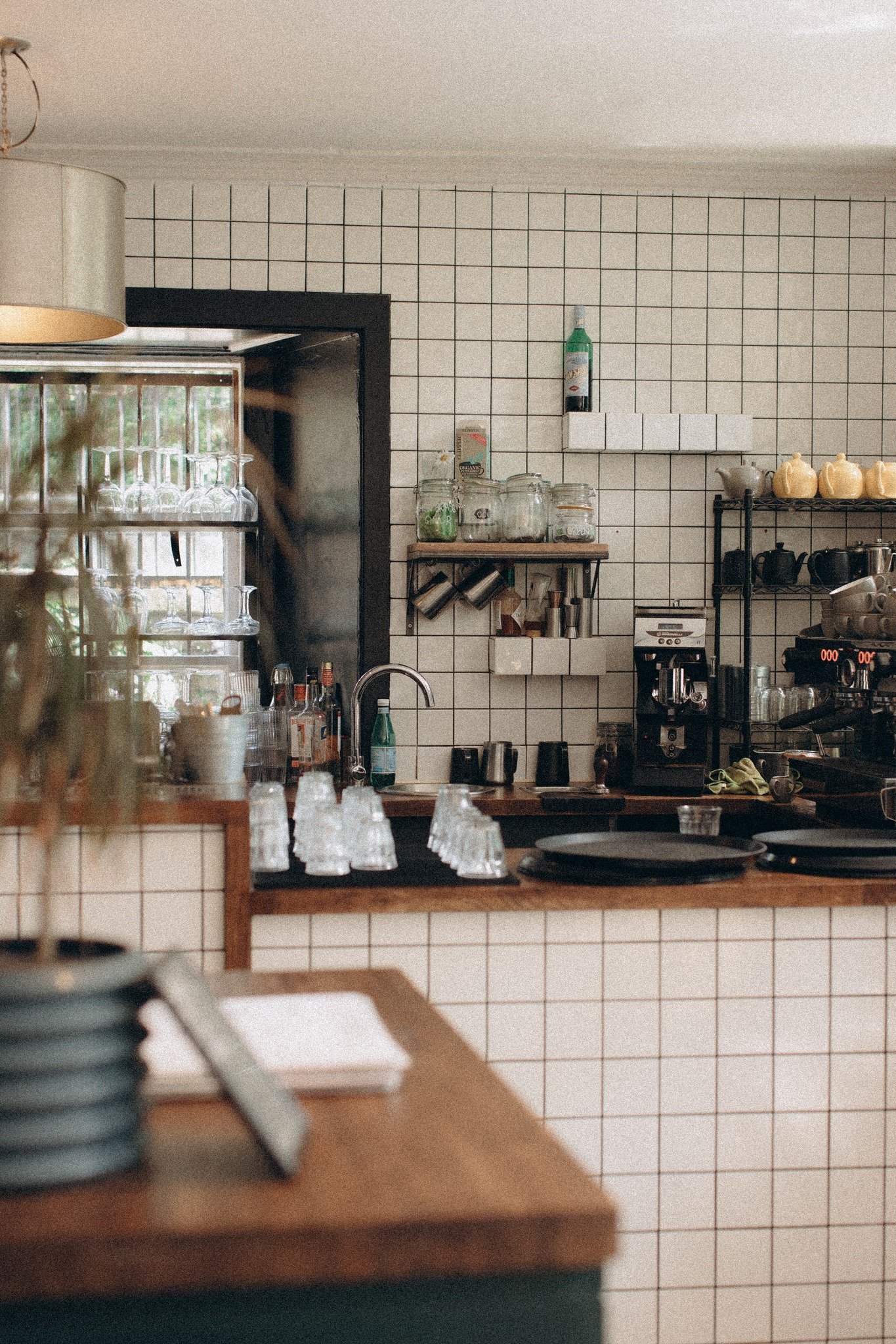 Interior of a cozy coffee shop with a tiled wall, shelves with jars and cups, and a coffee machine on the counter.  Interior Design Photography Chicago IL, Erin Drewitz Photography