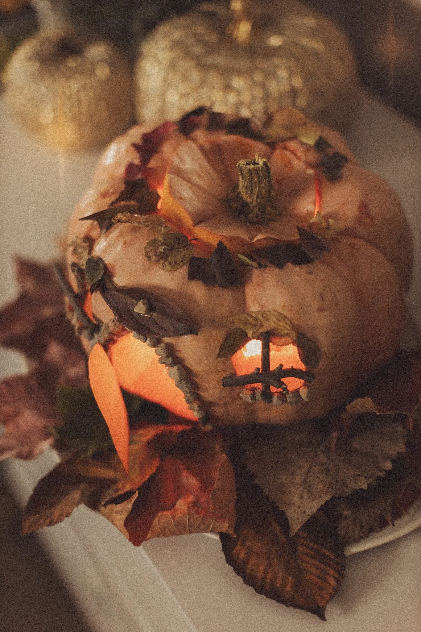 A carved pumpkin with a face, surrounded by autumn leaves and mini pumpkins, illuminated from within for a Halloween or fall display.  Product Photography Chicago IL, Erin Drewitz Photography
