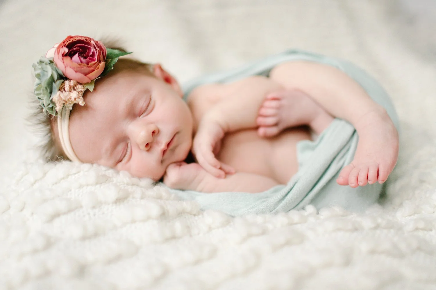 A sleeping newborn baby girl with a floral headband, resting on a soft, cream-colored blanket. Lifestyle newborn session shot in Evanston IL.
