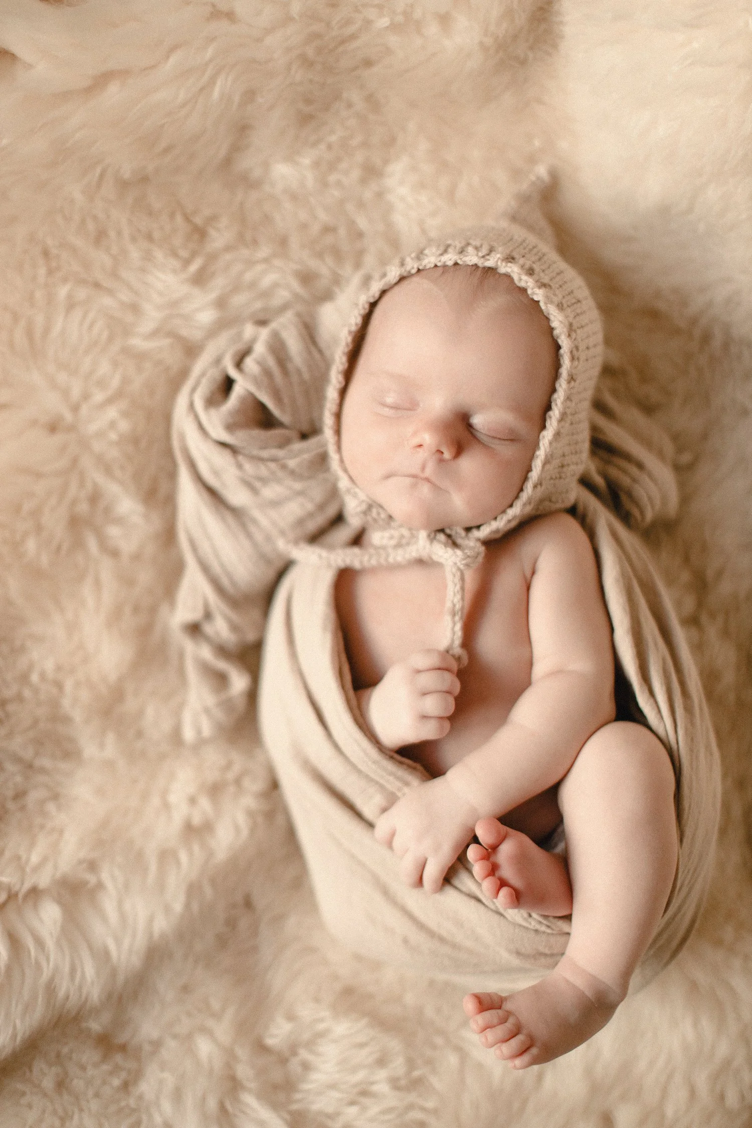 A sleeping baby with a bonnet and swaddle, lying on a soft, fluffy blanket.