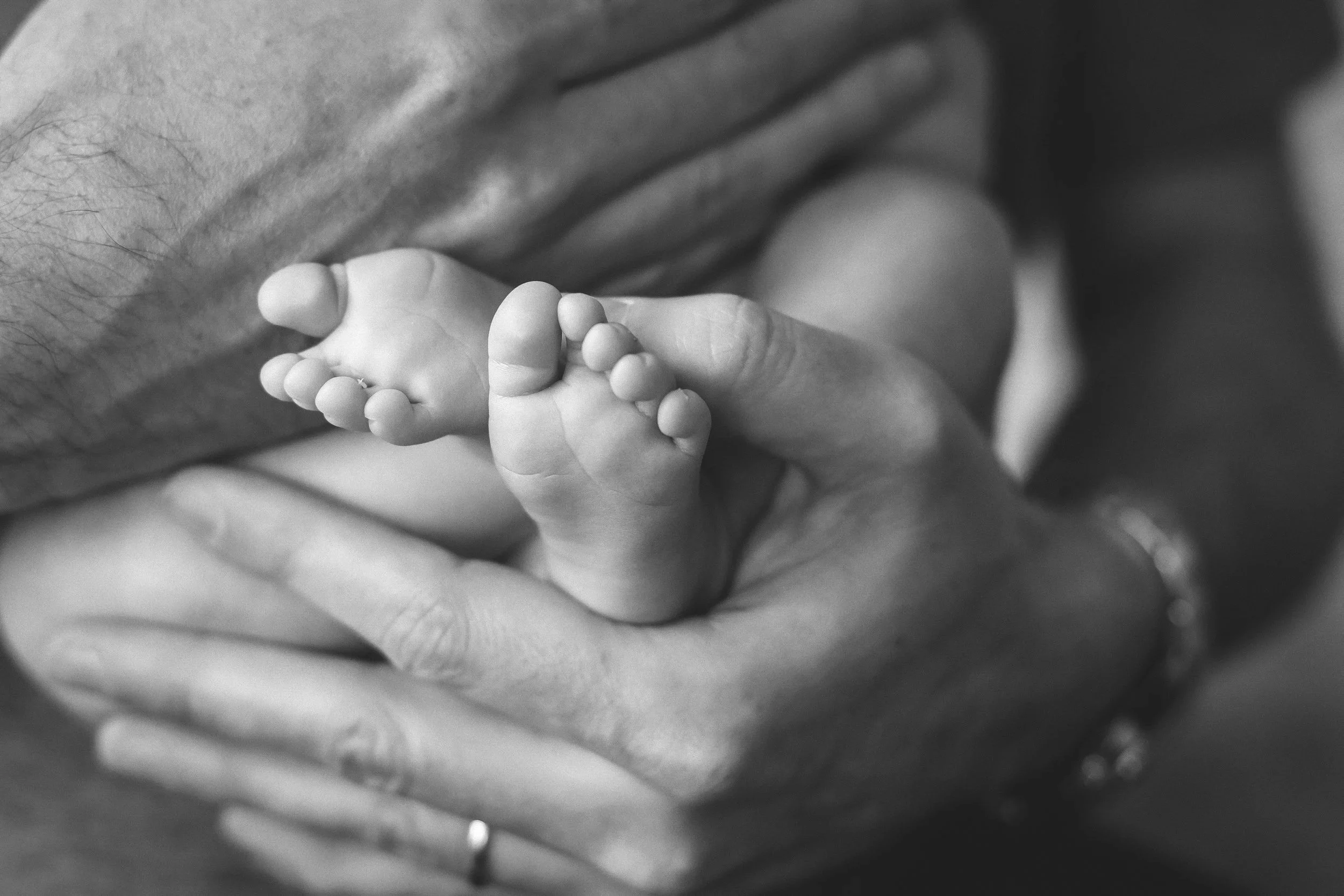 Close-up of an adult hand gently holding a tiny, newborn baby's foot on a blanket, in black and white.