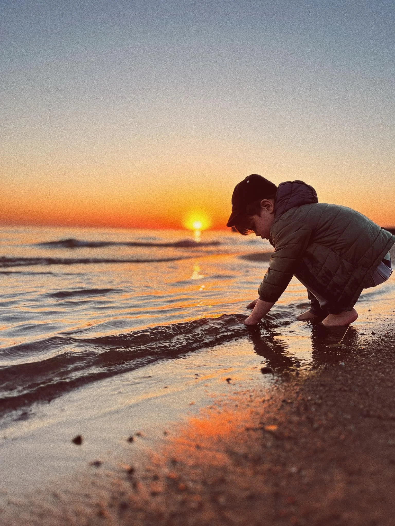 A young boy playing in the shallow water at the beach during sunset.
