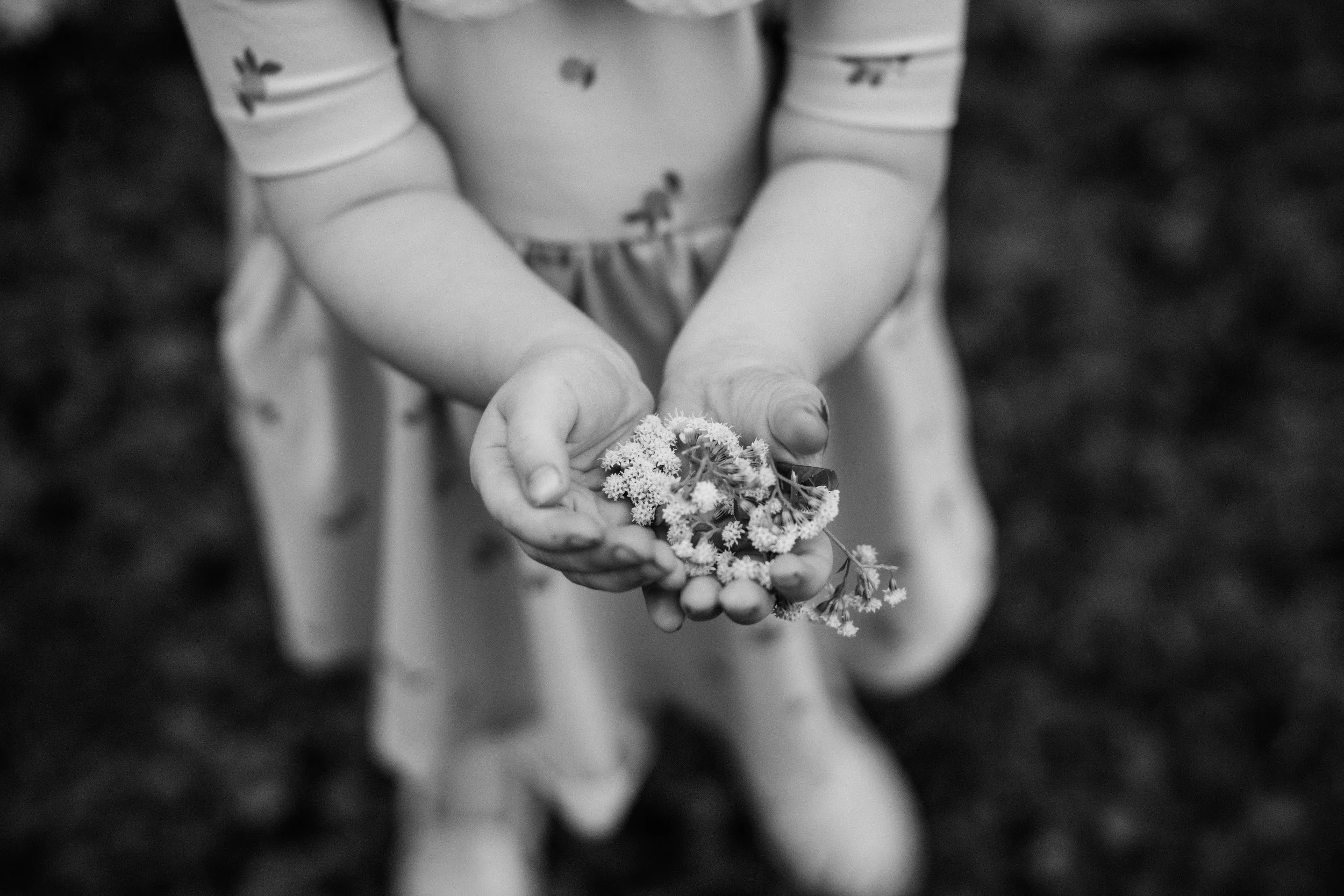 A child in polka dot dress holding a small bunch of flowers in both hands.