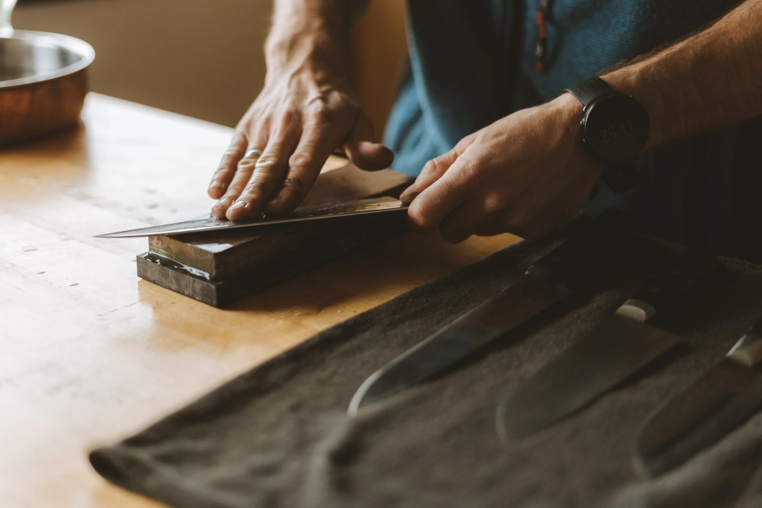 Person sharpening a knife on a whetstone on a wooden workbench.