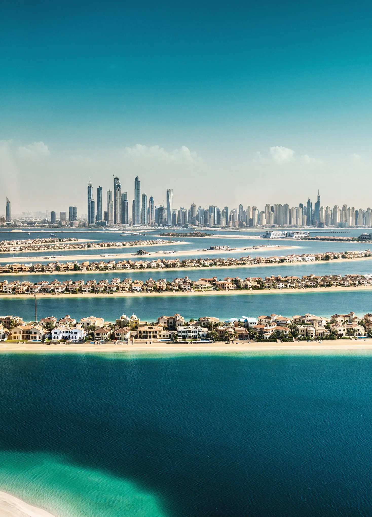 Panoramic view of Dubai skyline with high-rise buildings, a body of water, and residential houses in the foreground.