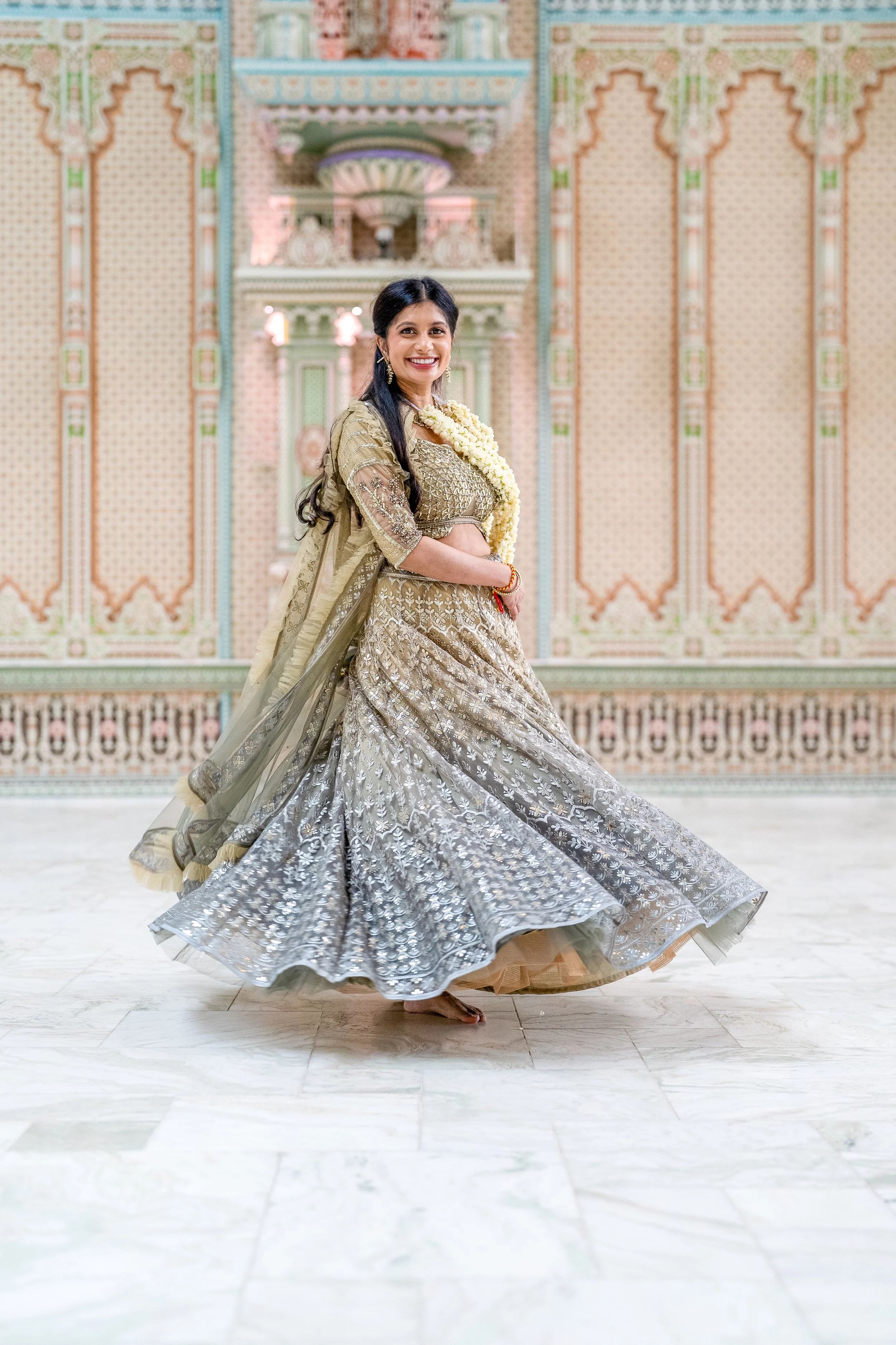 A woman in traditional Indian attire is dancing in an ornately decorated hall with intricate wall patterns and a central niche or altar.