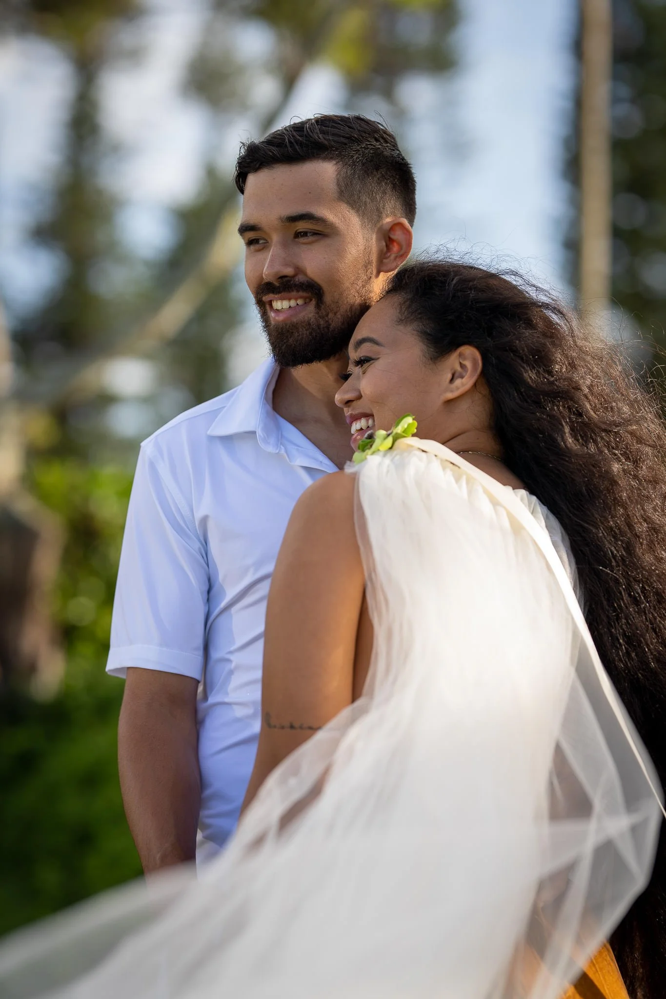 A happy couple is outdoors, embracing and smiling, with trees in the background.