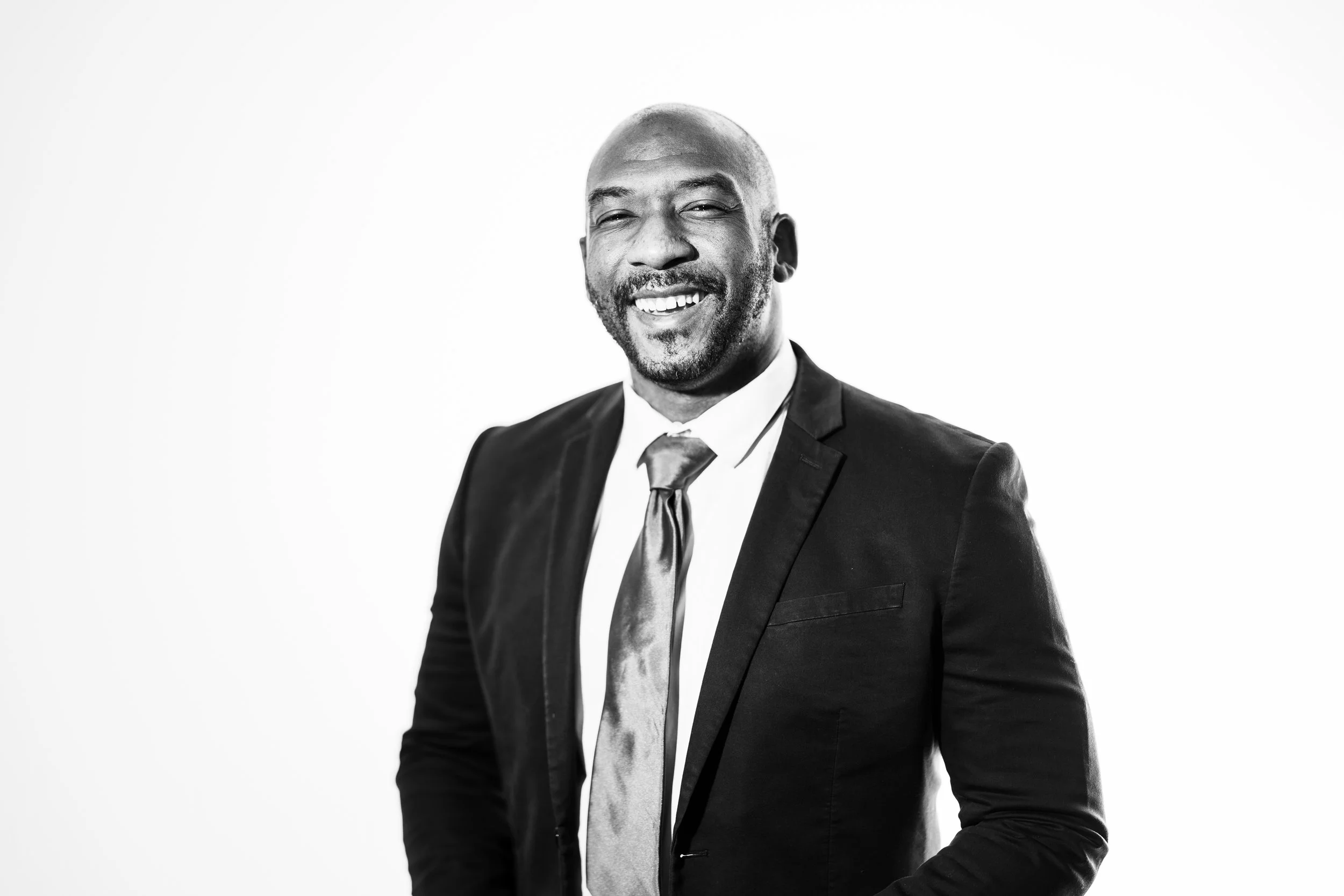 Black and white portrait of a smiling man in a suit and tie, with a plain white background.
