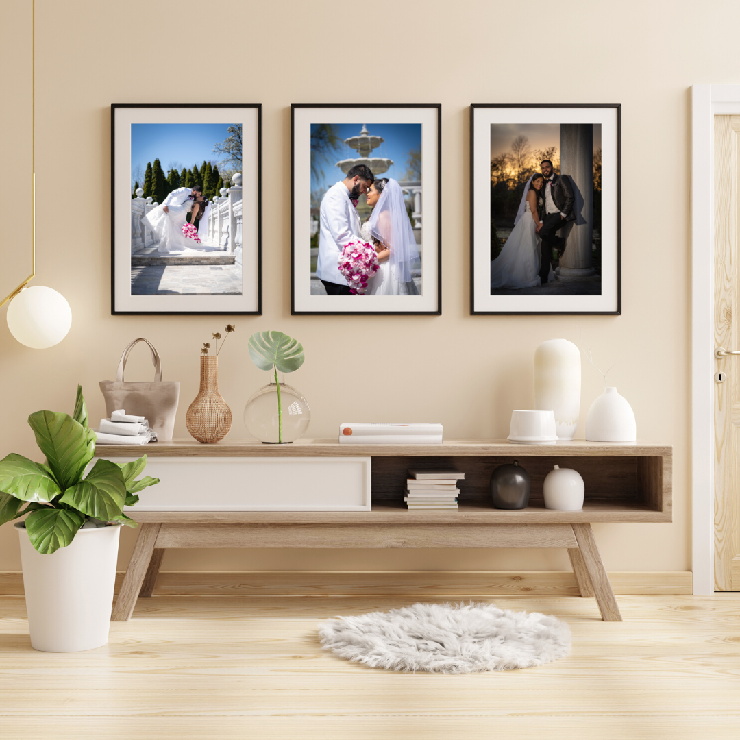 Decorative wall with three framed wedding photographs, a wooden sideboard with vases, books, and decor, a large green plant in a white pot, and a fluffy white rug.