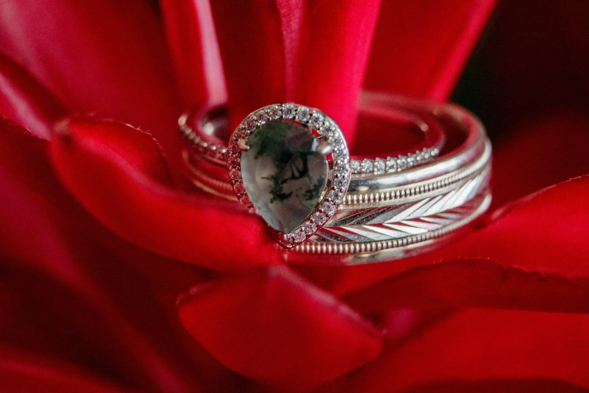 Three silver rings, one with a heart-shaped black gemstone surrounded by small diamonds, placed on red flower petals.
