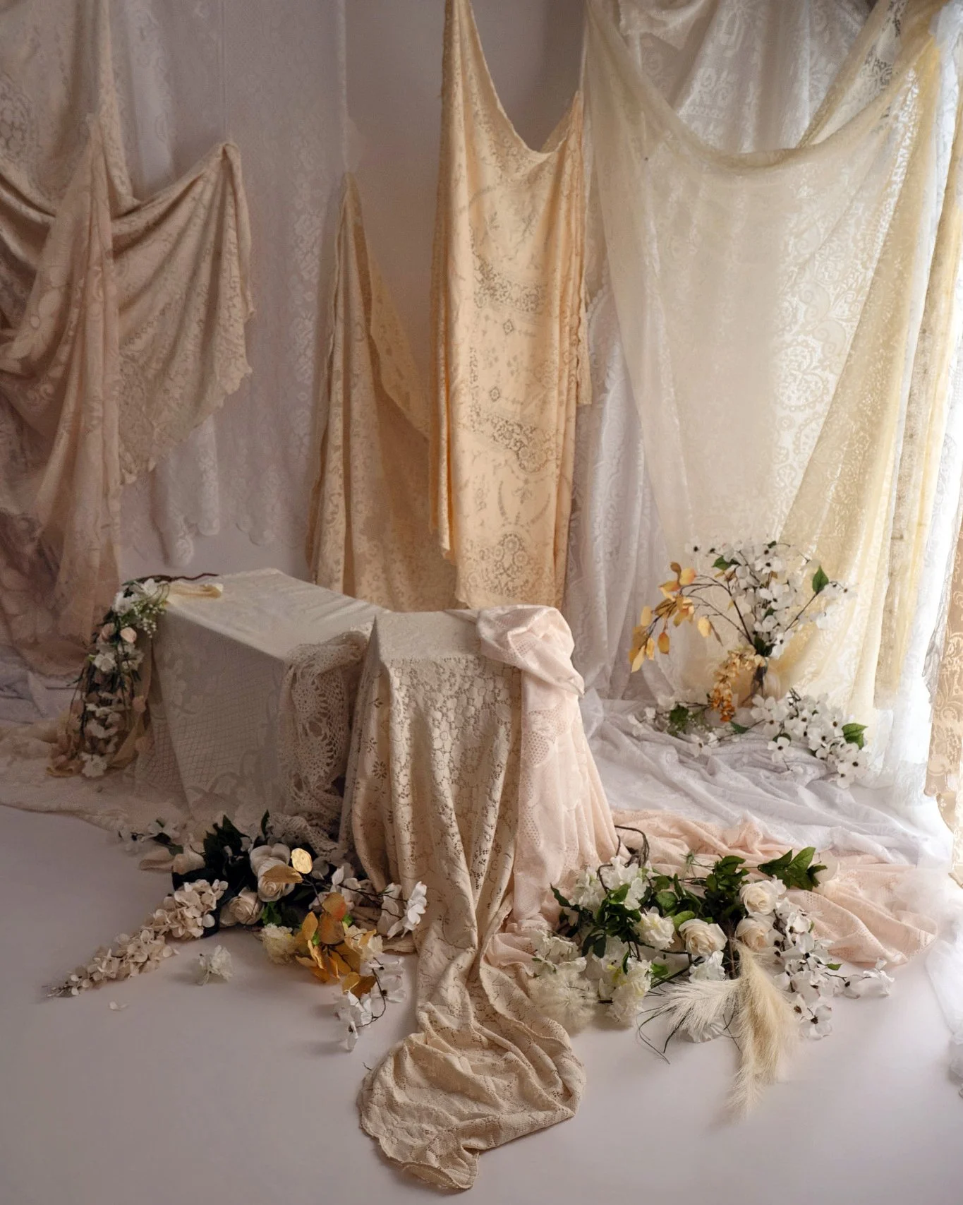 In studio set up with soft lighting, vintage lace fabrics and florals in shades of cream and white