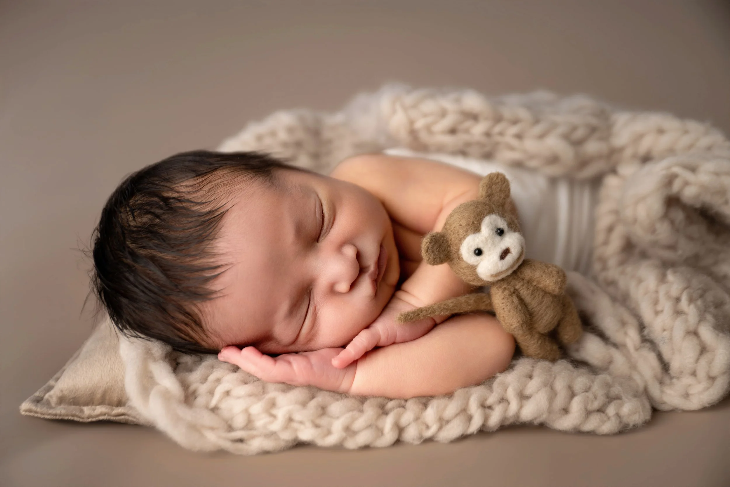 Newborn baby sleeping with hands on face holding small toy in Modesto CA