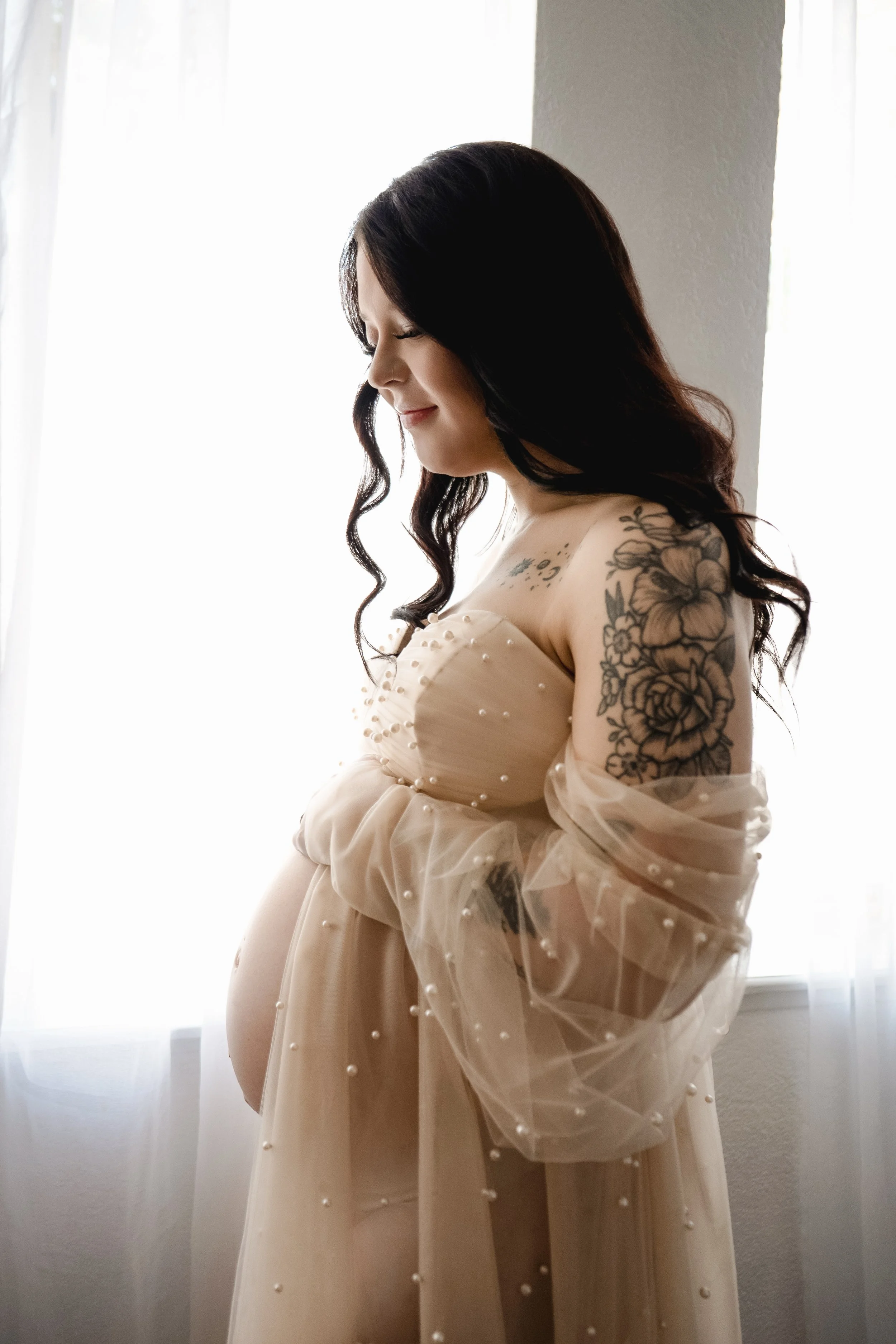 Pregnant mother standing in front of a window with soft backlighting during a maternity photography session.