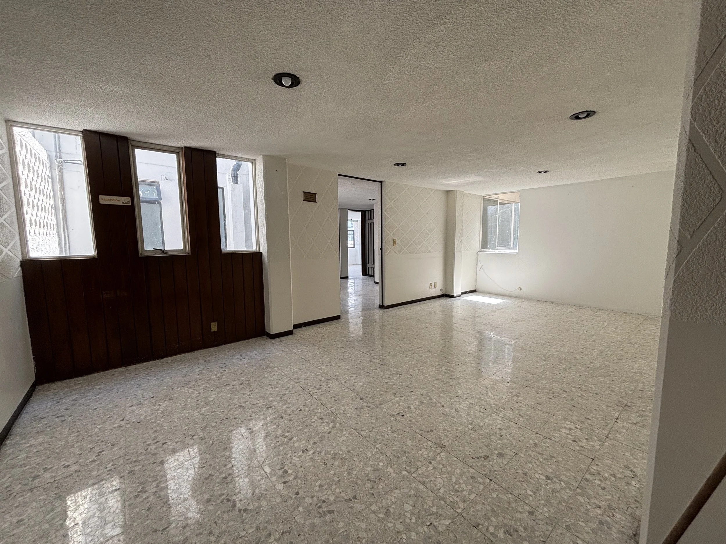 Empty living room with terrazzo flooring, white walls, and windows letting in natural light.