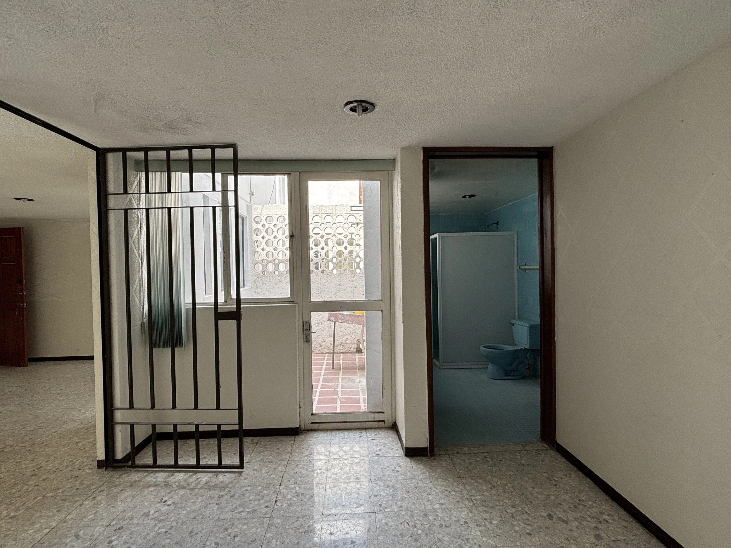 Interior view of an apartment with a door leading to an outdoor patio, a bathroom with blue walls, and a metal security gate.