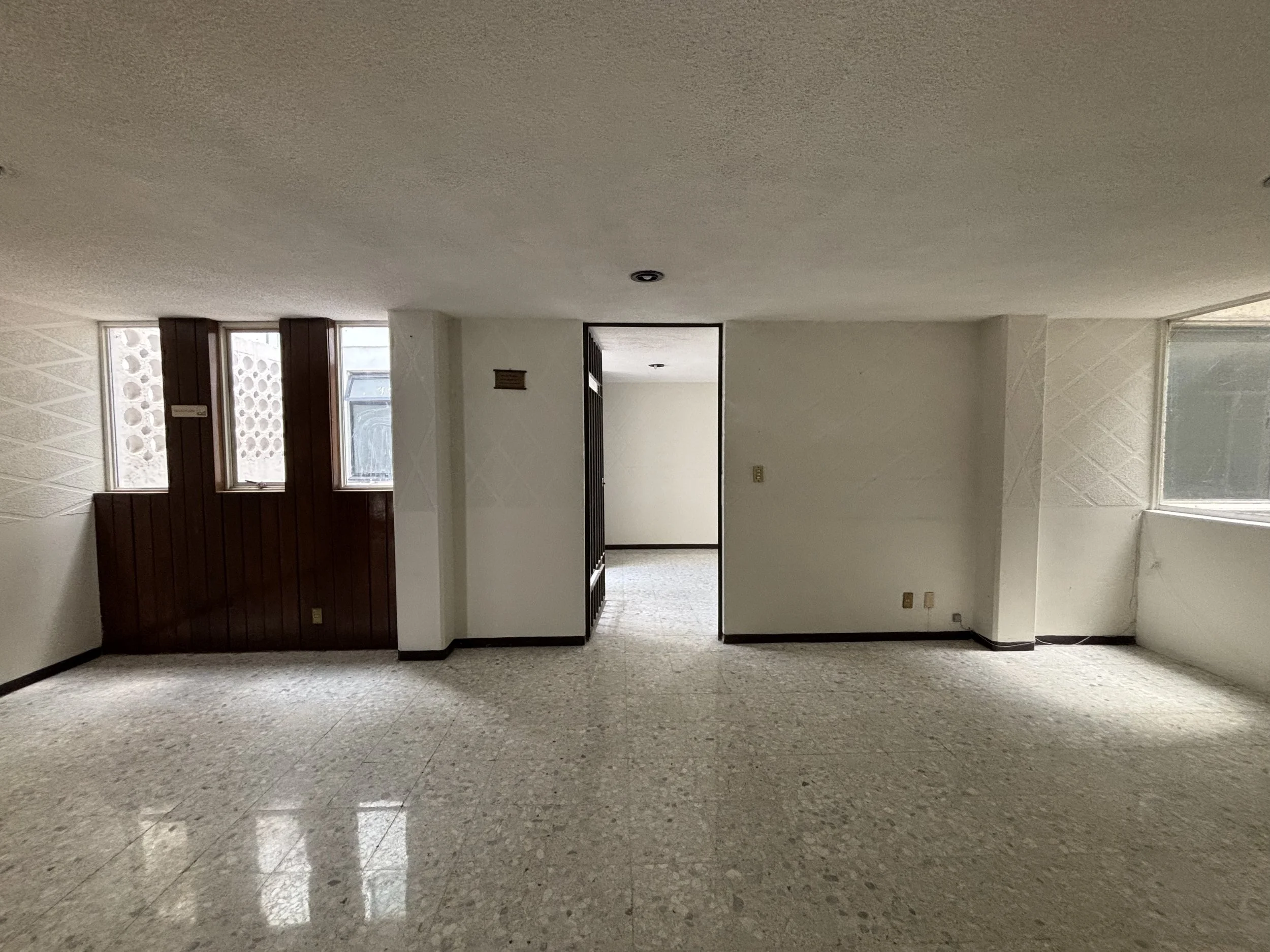 Empty living room with beige walls, large windows, and a polished stone floor.