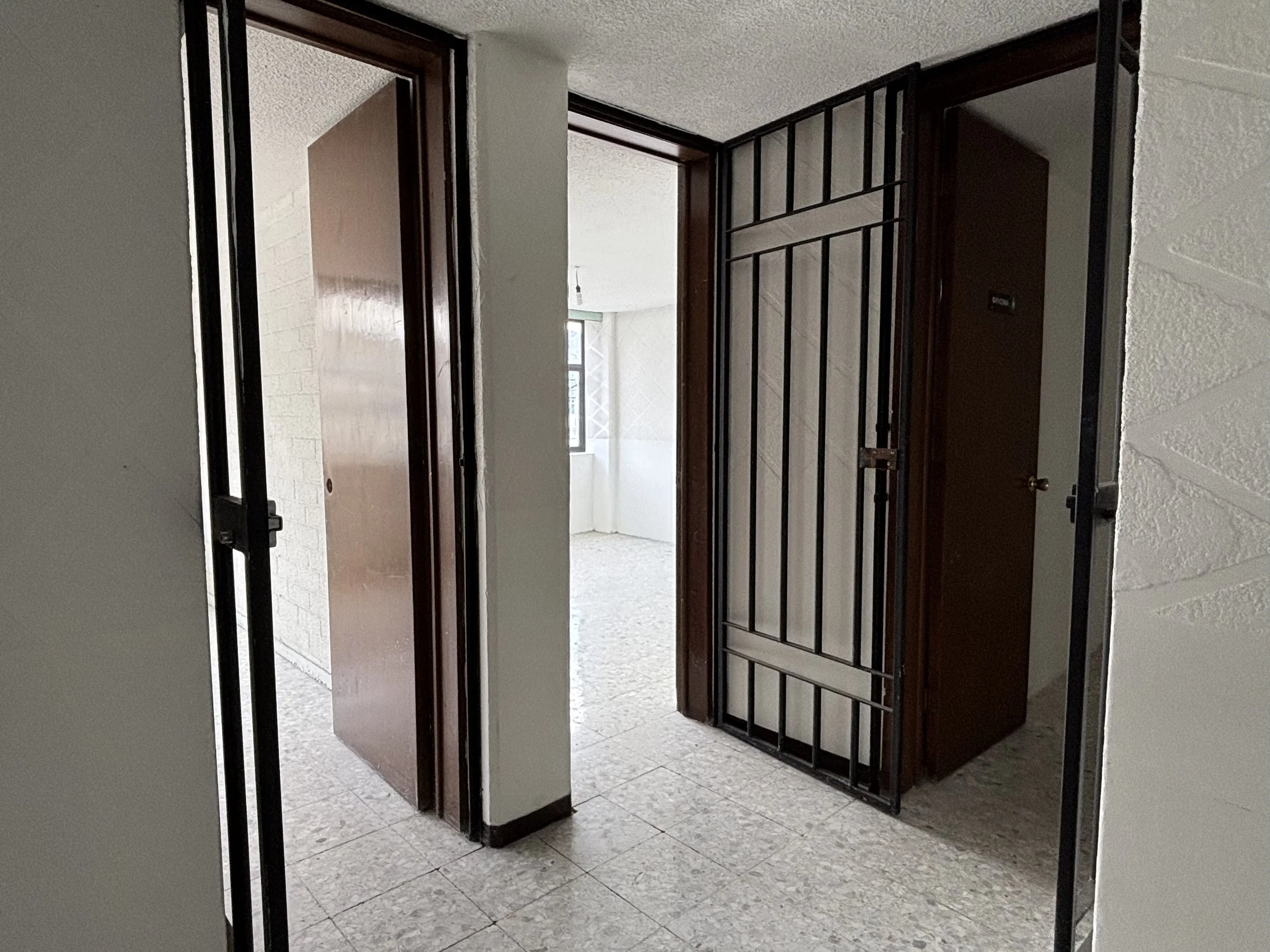 View of an apartment entrance with brown doors, a security gate, and a living area visible through the open door, with tiled floors and a window.