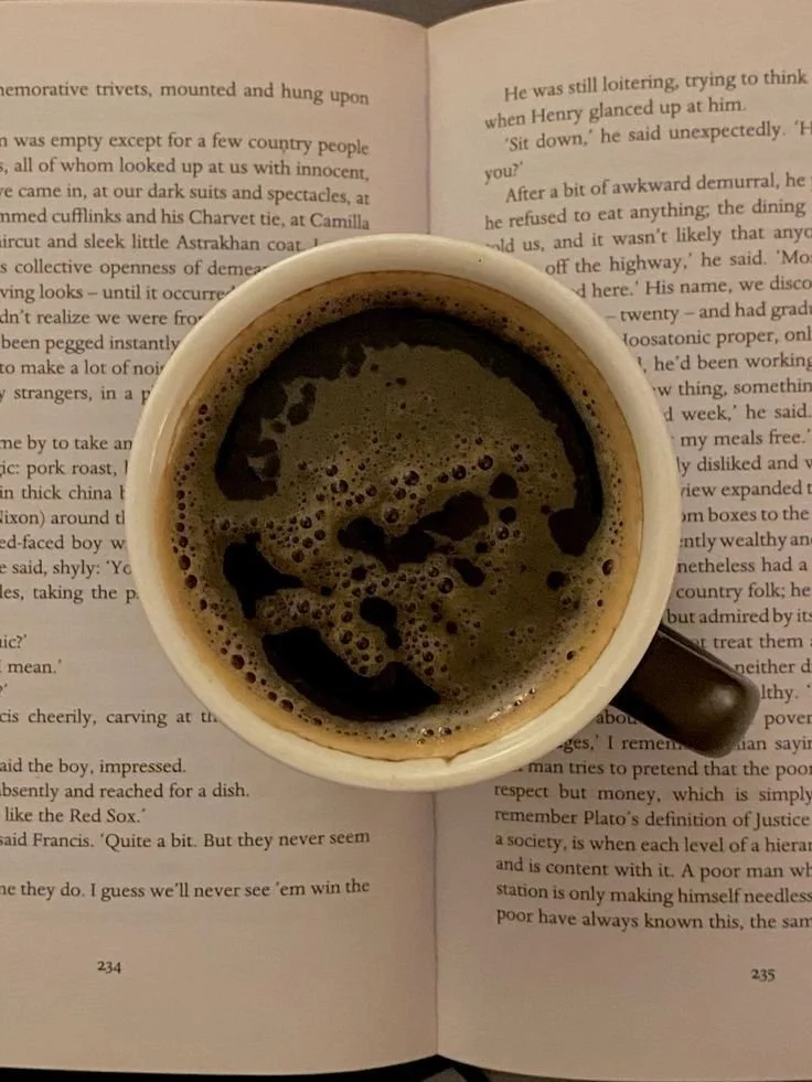 A top-down view of a cup of black coffee on open book pages.