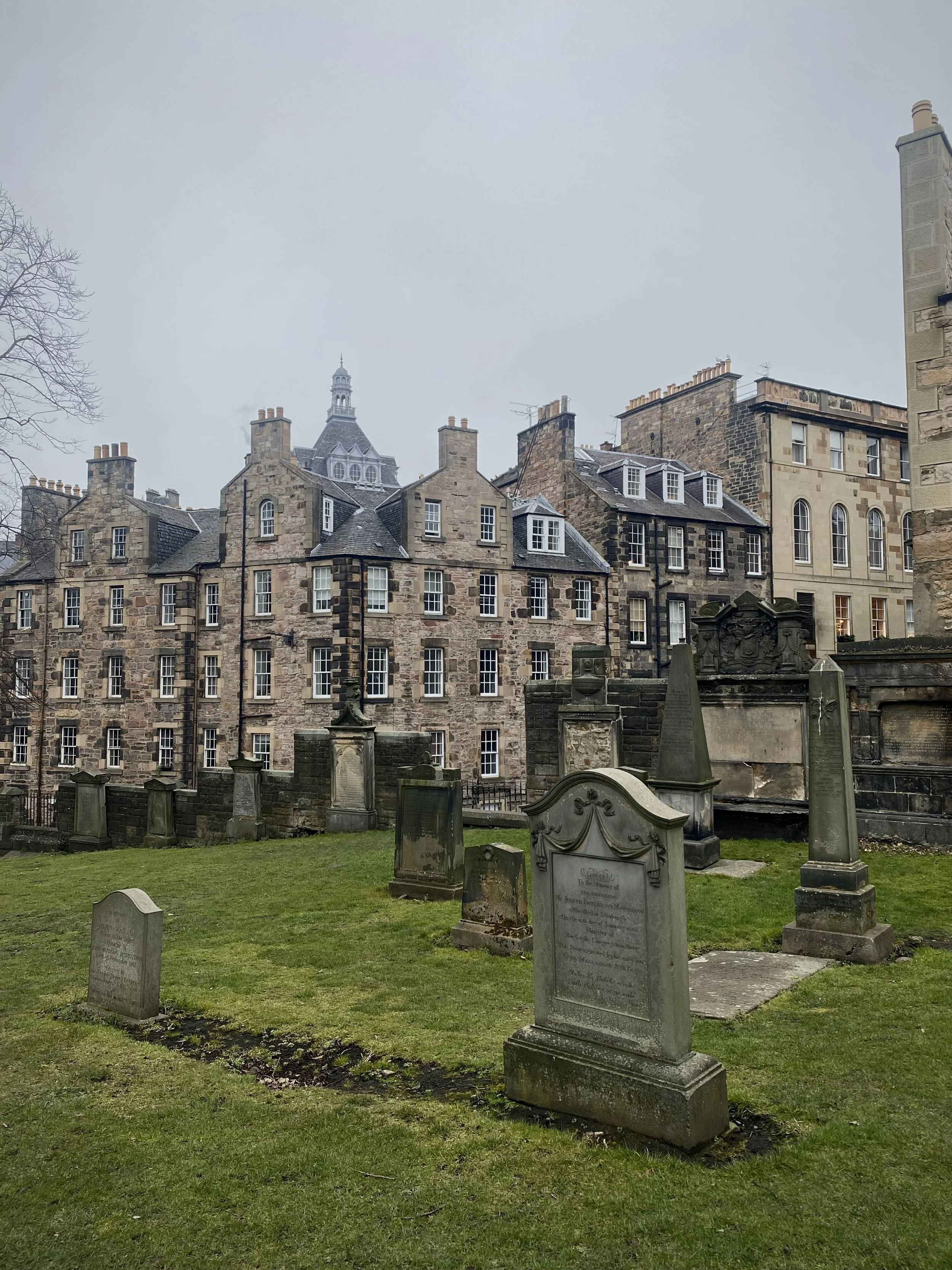 Historic stone buildings and a cemetery with old gravestones in the foreground on a cloudy day.