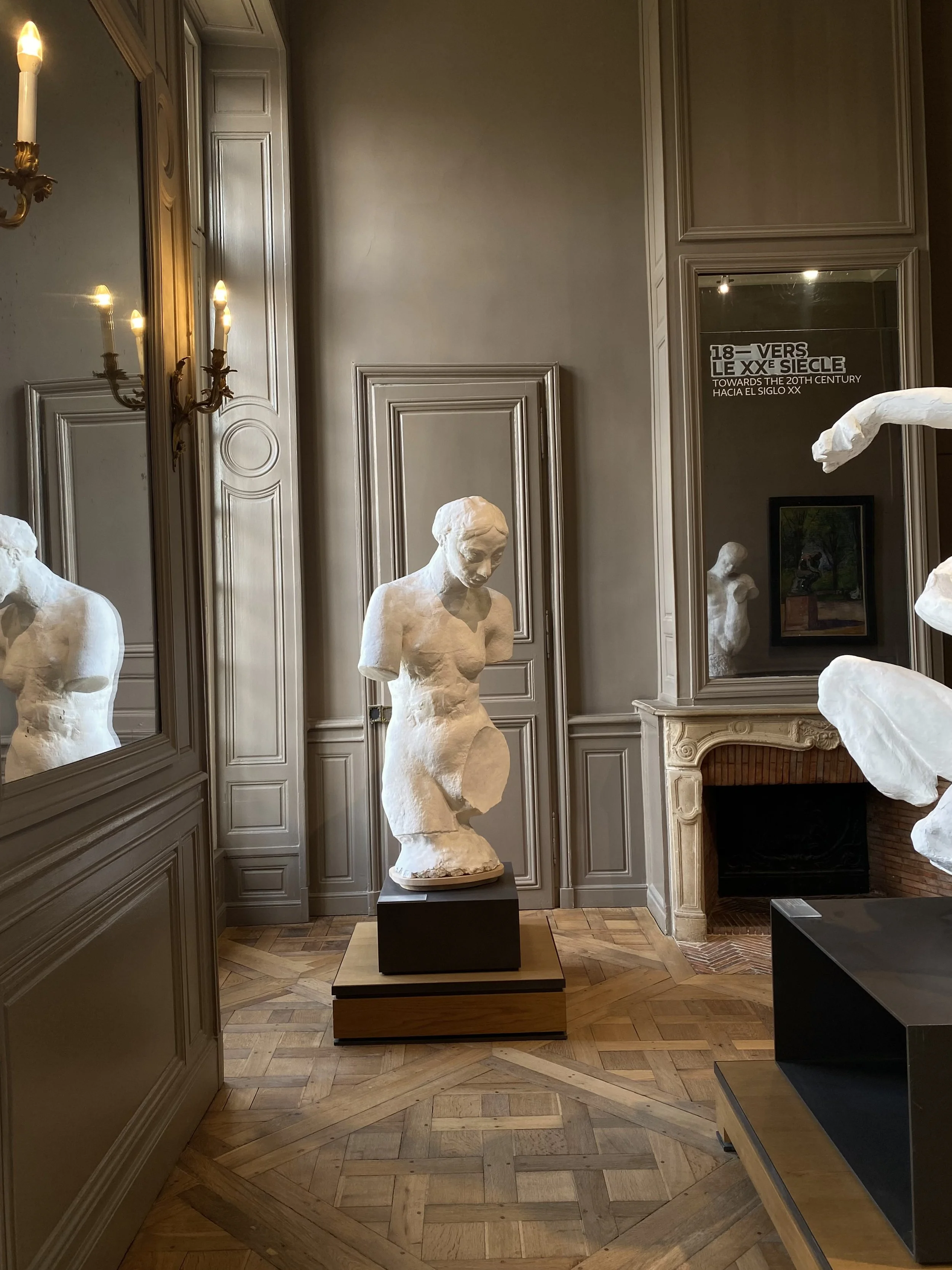 Art museum interior with marble bust sculptures, ornate wall paneling, a fireplace, and a mirror with text about 19th-century art.