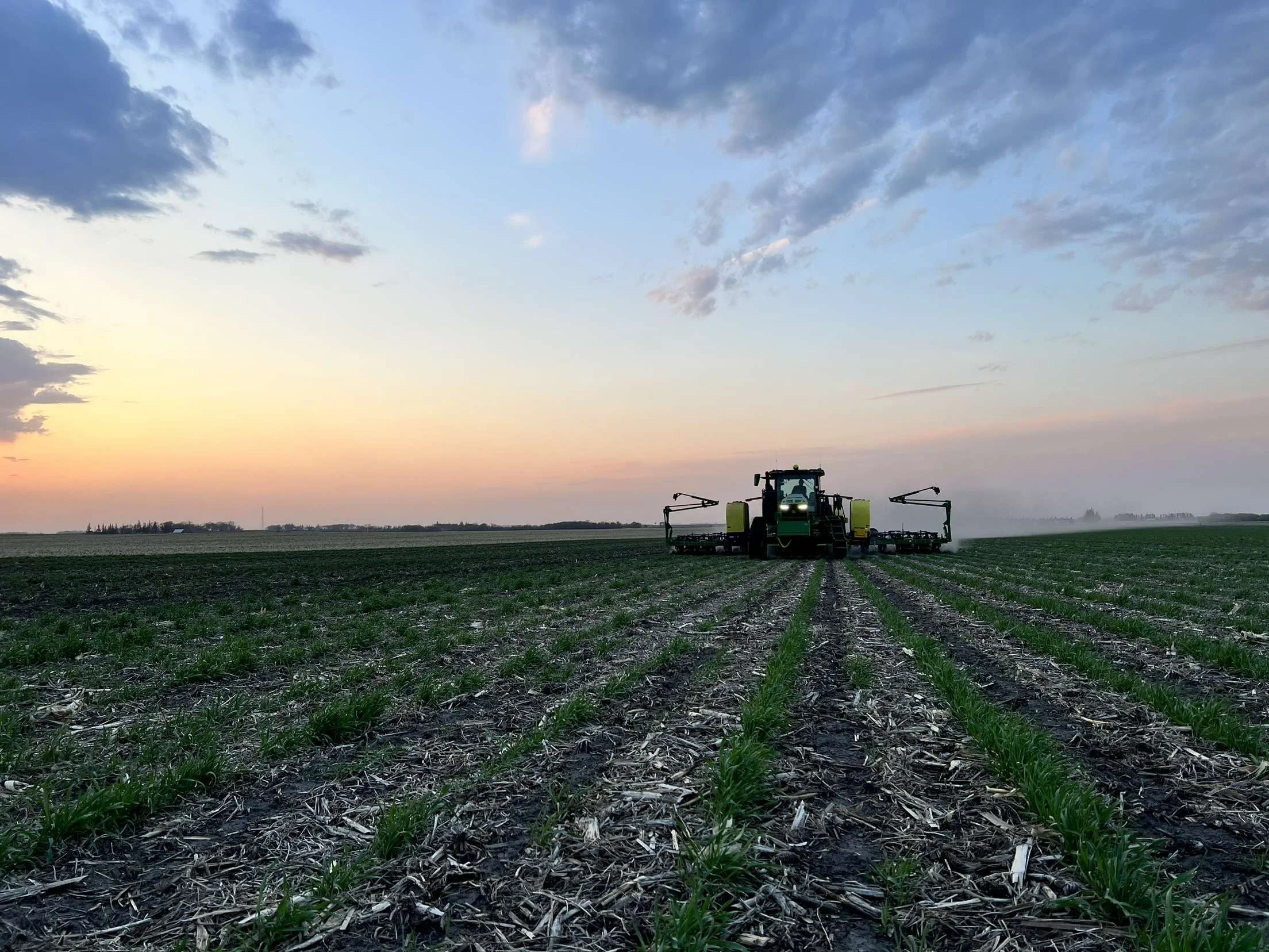 A tractor working in a field during sunset, with a sky of partly cloudy blue and soft orange hues.