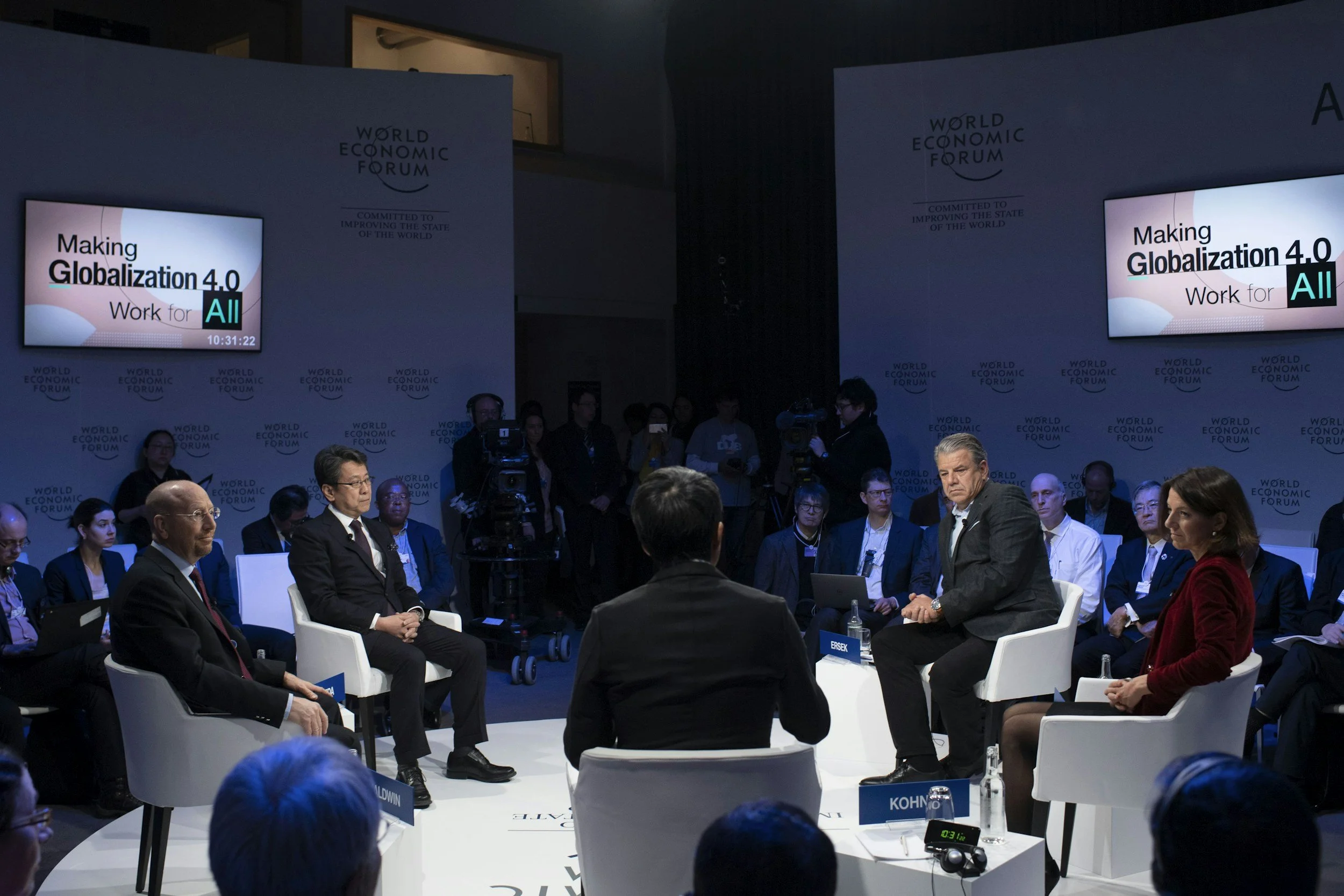 A panel discussion at the World Economic Forum with several participants seated in a circle, with two large screens displaying the text "Making Globalization 4.0 Work for All."