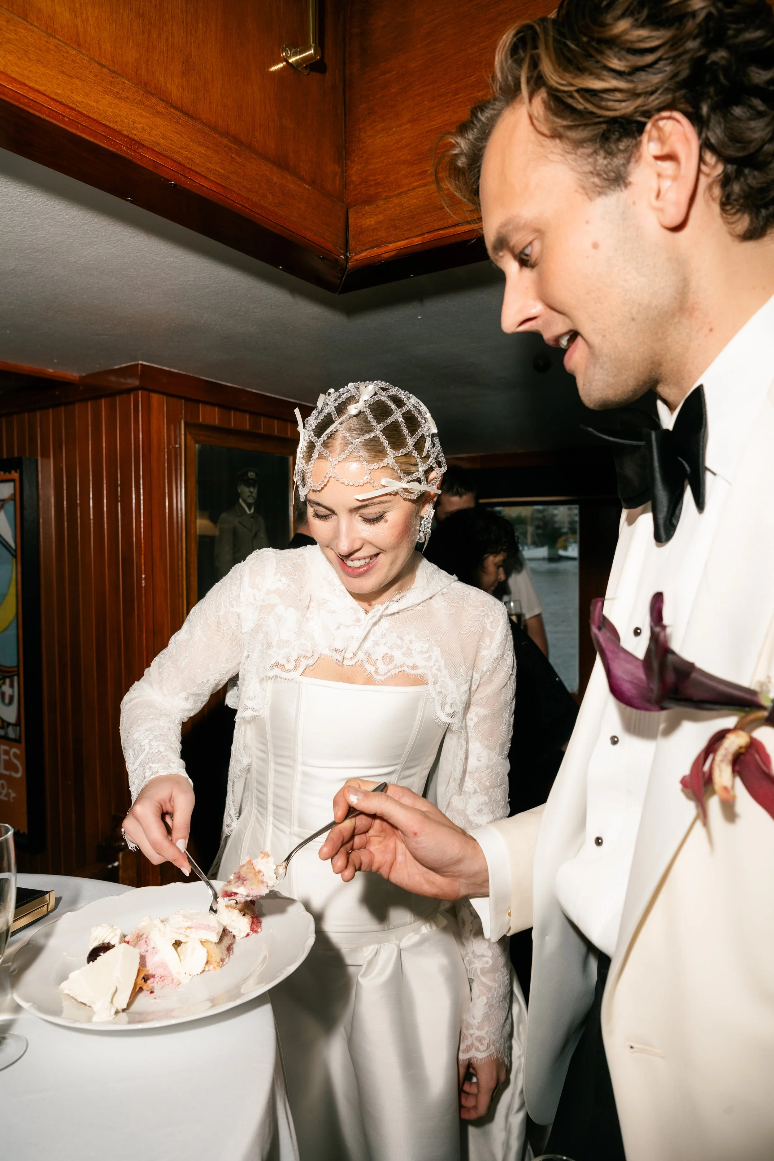 A bride and groom in wedding attire sharing a slice of cake at their wedding reception, both smiling.