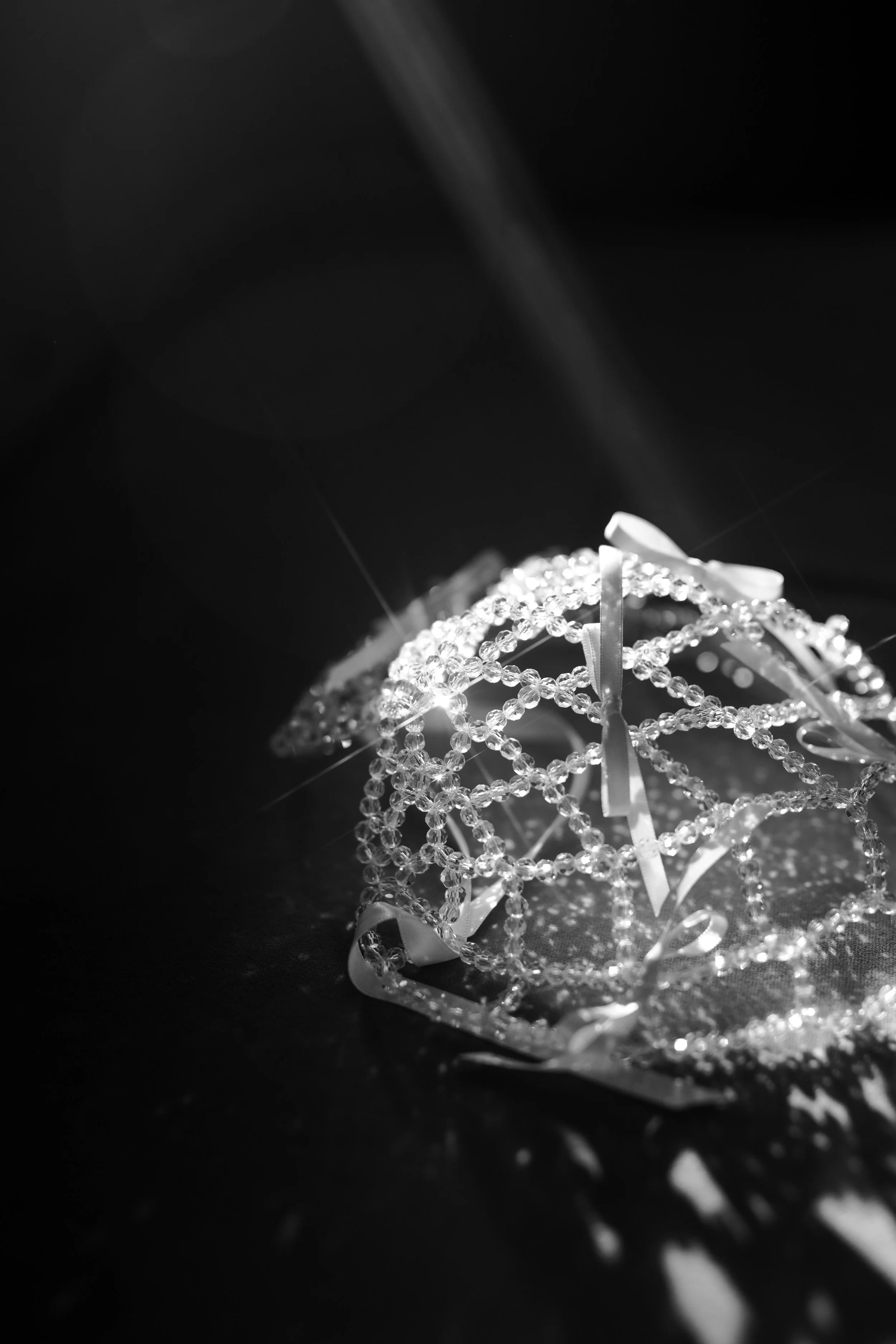 A decorative ball made of sparkling beads and ribbons on a dark surface with light reflections.