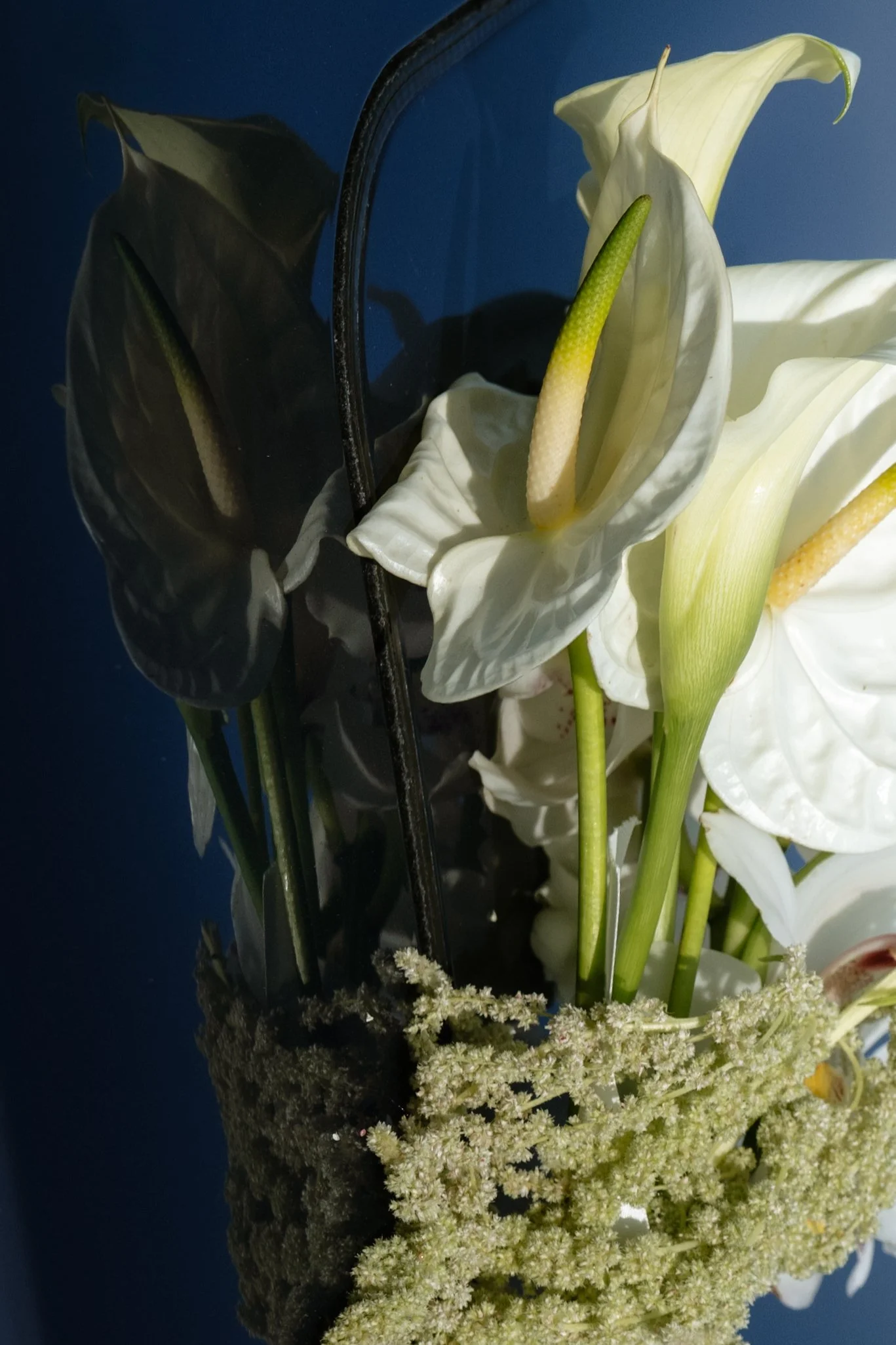 White and dark-colored calla lilies arranged in a bouquet with a dark background.