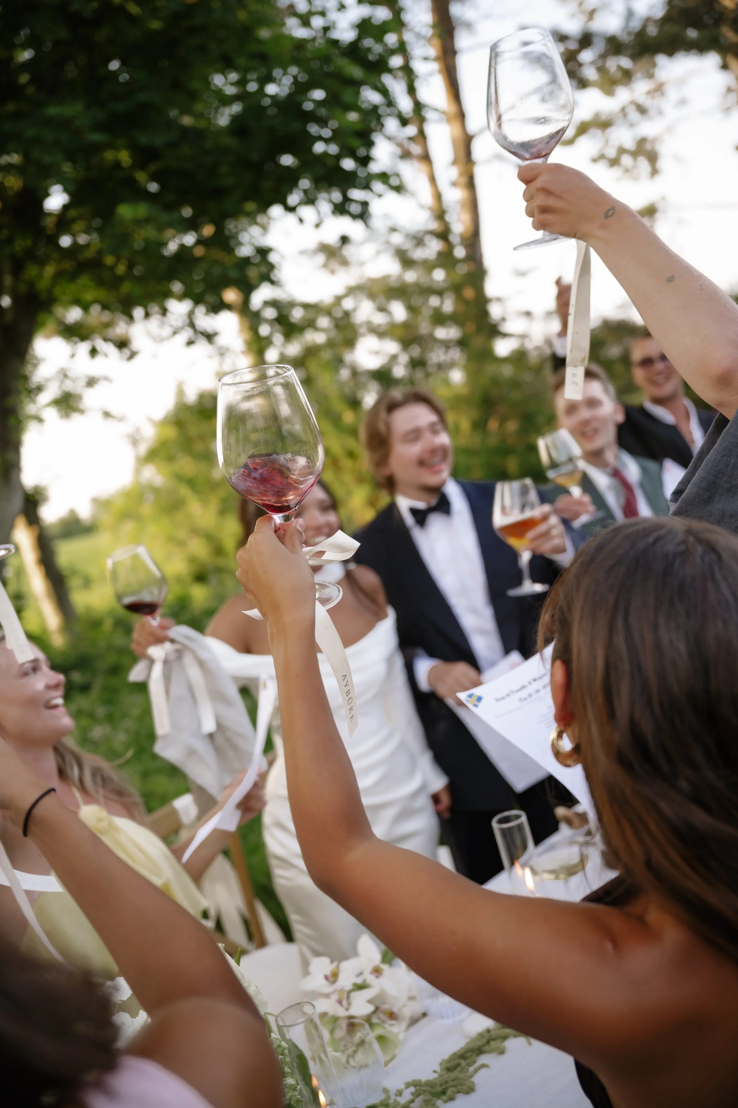 People celebrating outdoors at a wedding, raising glasses of wine and champagne, with trees in the background.