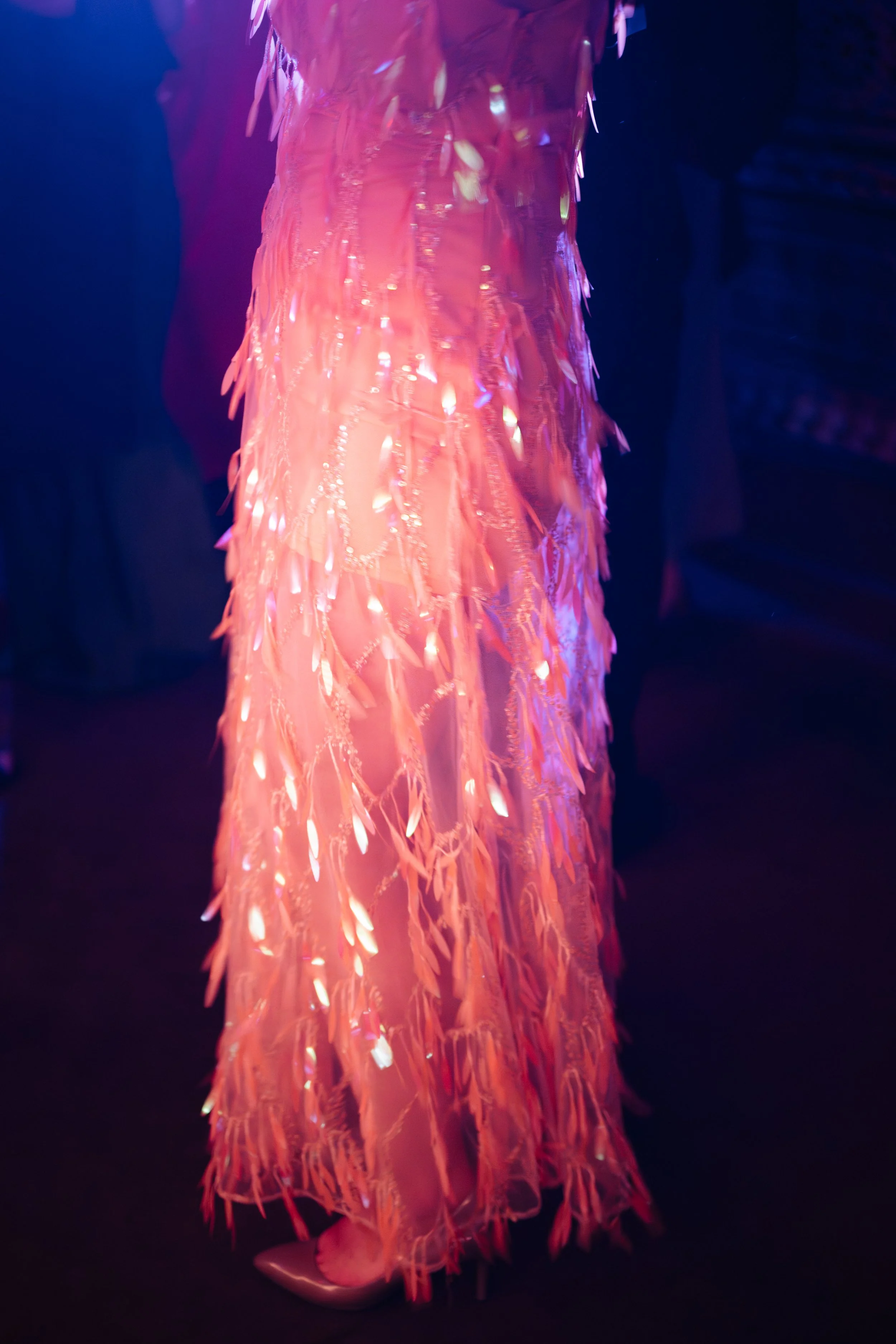 Close-up of a person wearing a long pink dress decorated with shimmering, feather-like sequins.