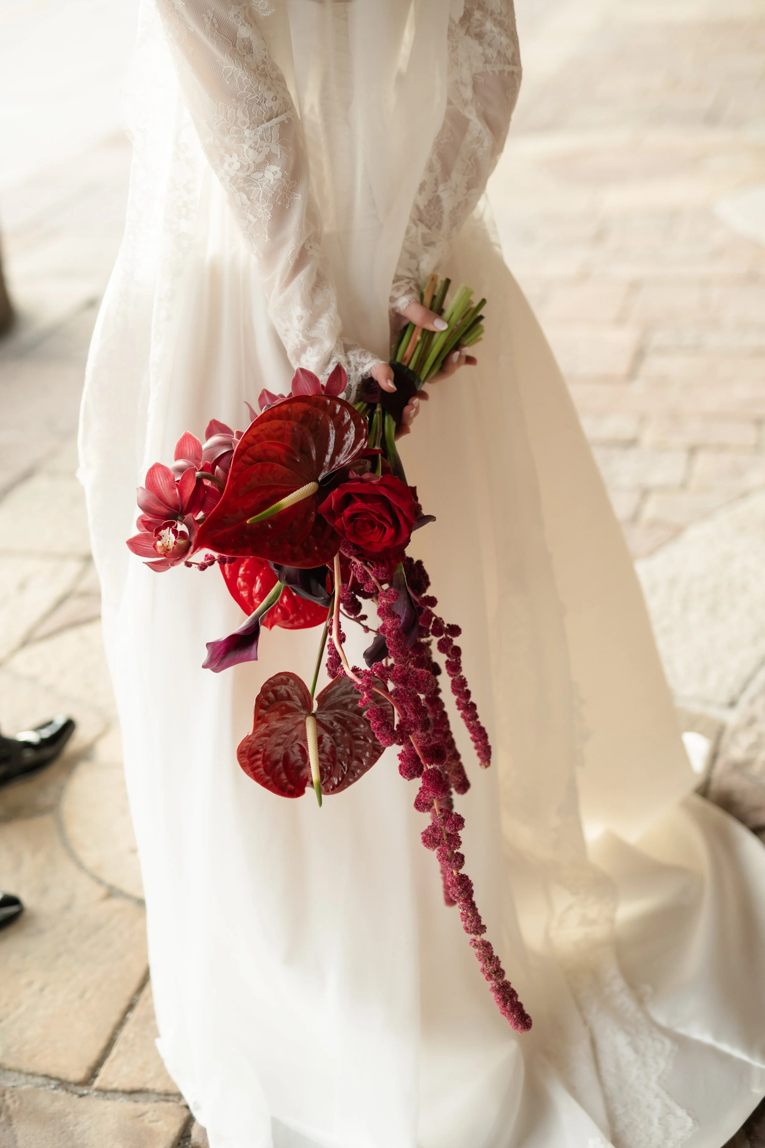 Bride in a white wedding dress holding a cascading bouquet of red and purple flowers, including roses, orchids, and anthuriums.
