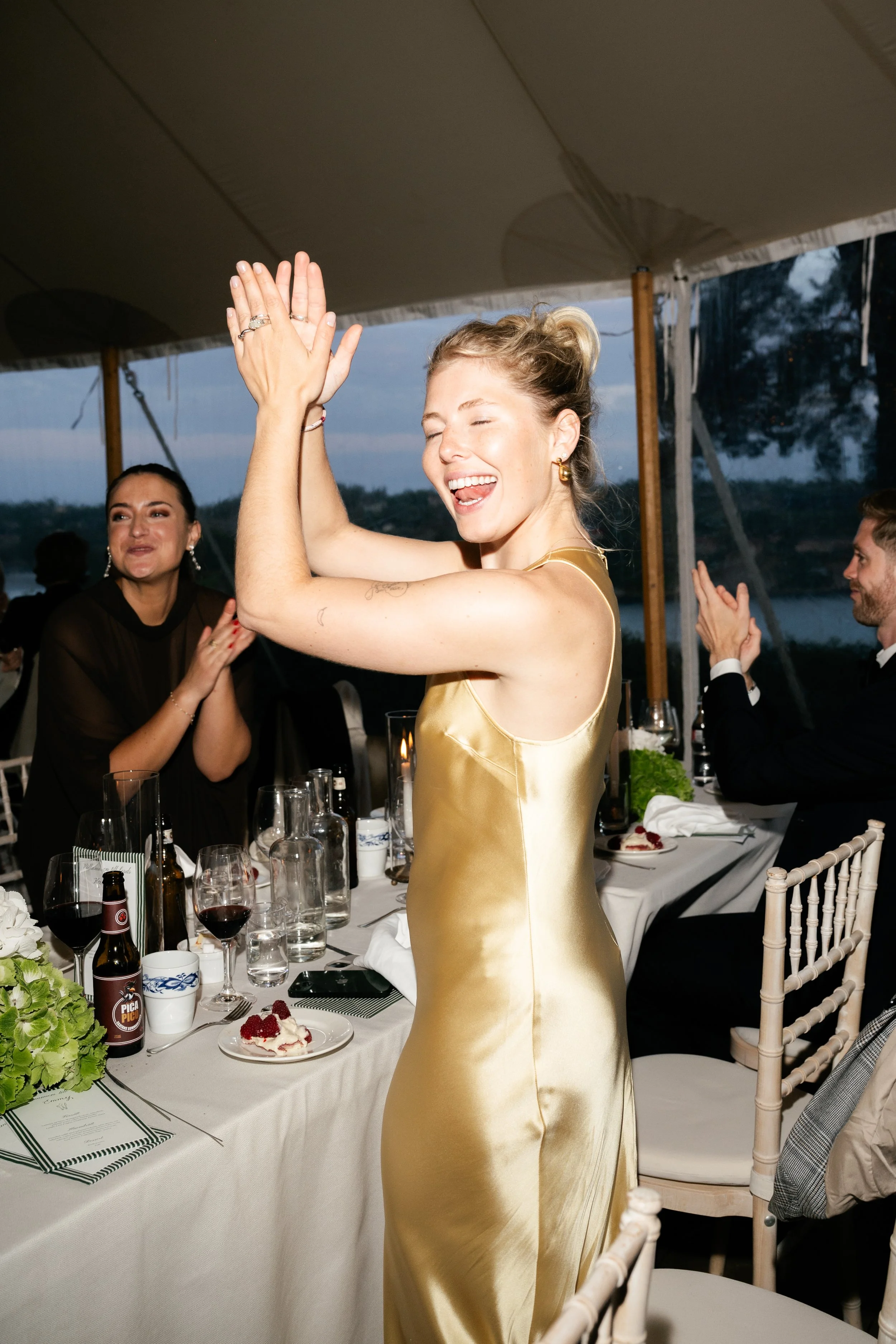 A woman in a gold satin dress dancing and clapping at a celebration dinner event.