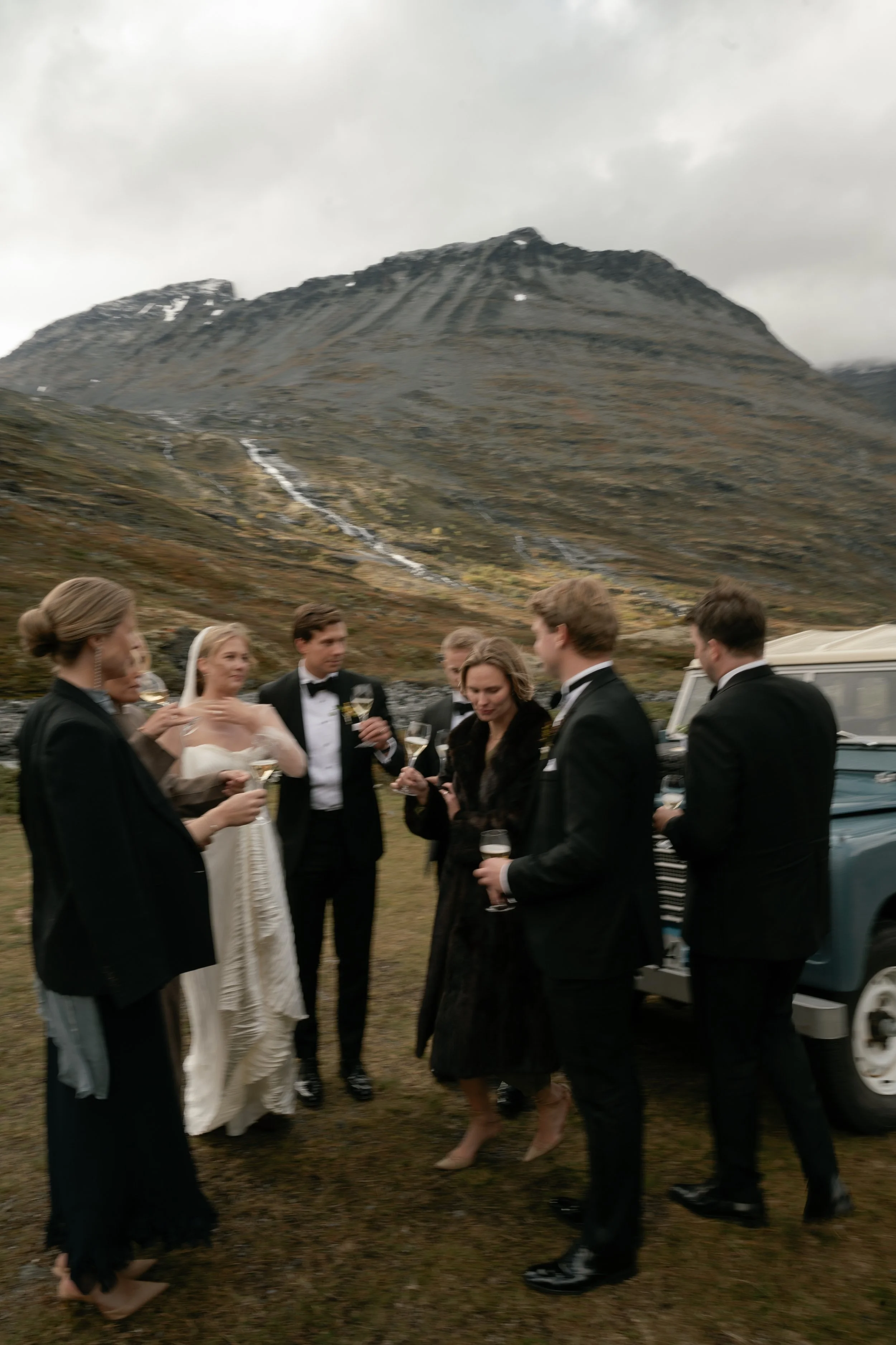 Group of people in formal attire enjoying drinks outdoors with mountainous landscape in the background