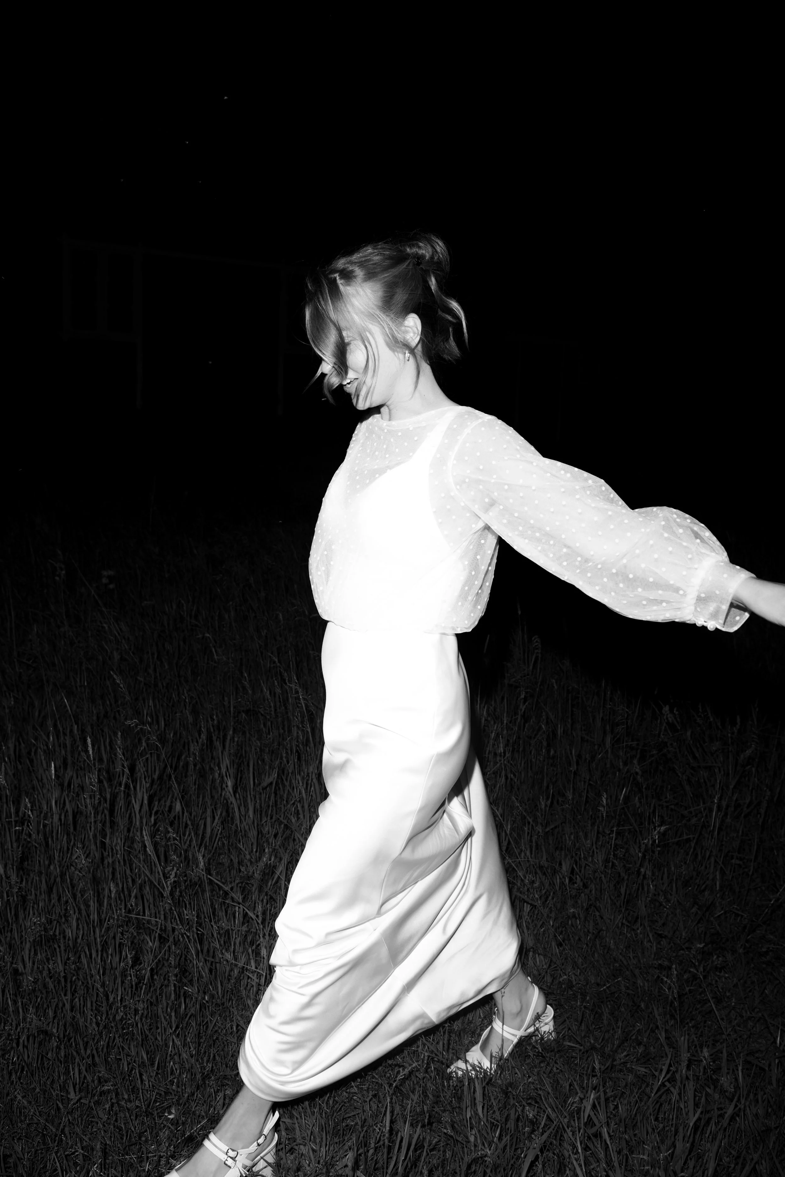 A woman in a white dress and high heels dancing outdoors at night.