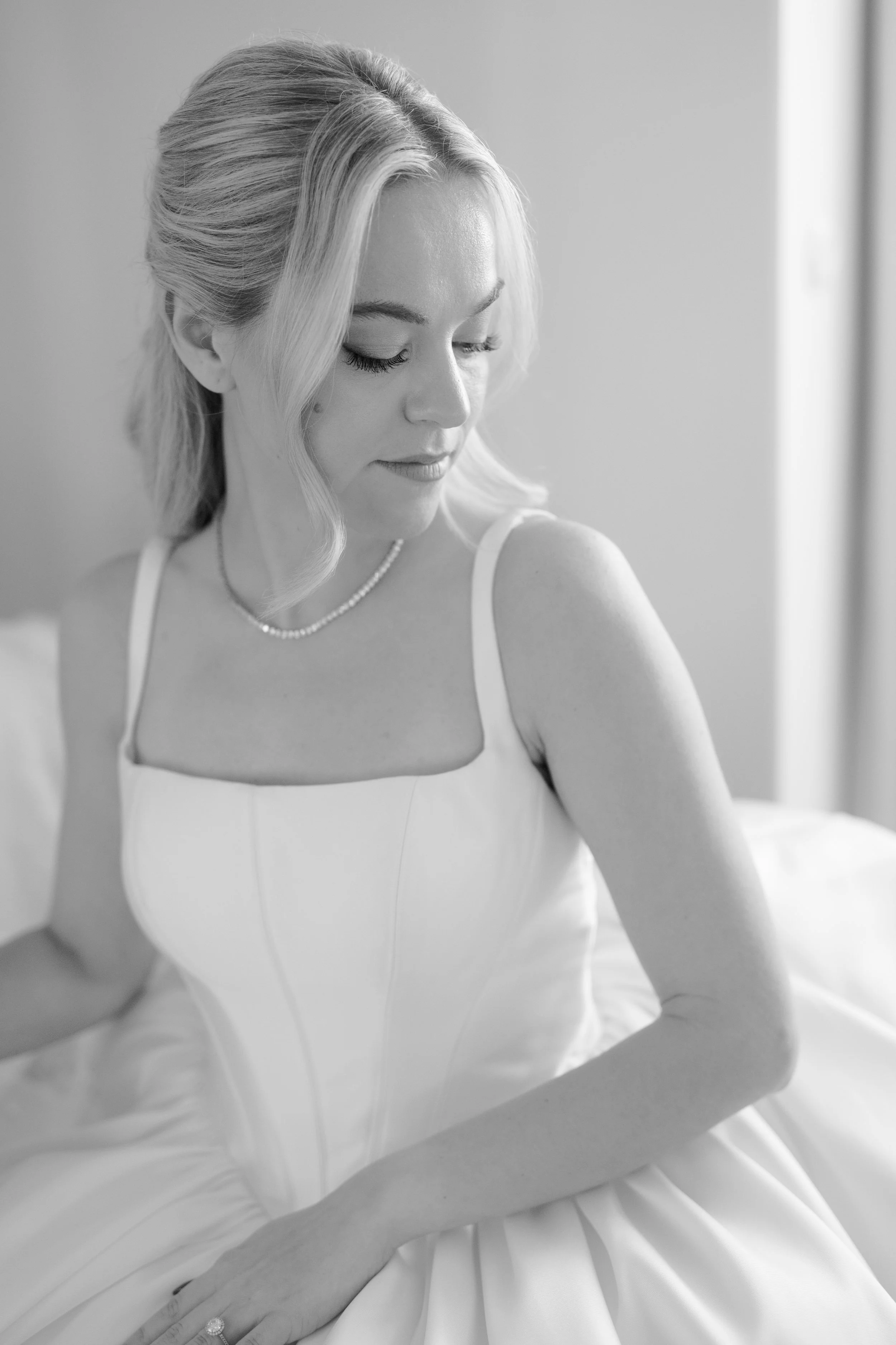 Black and white photo of a woman in a wedding dress looking down, sitting on a bed.