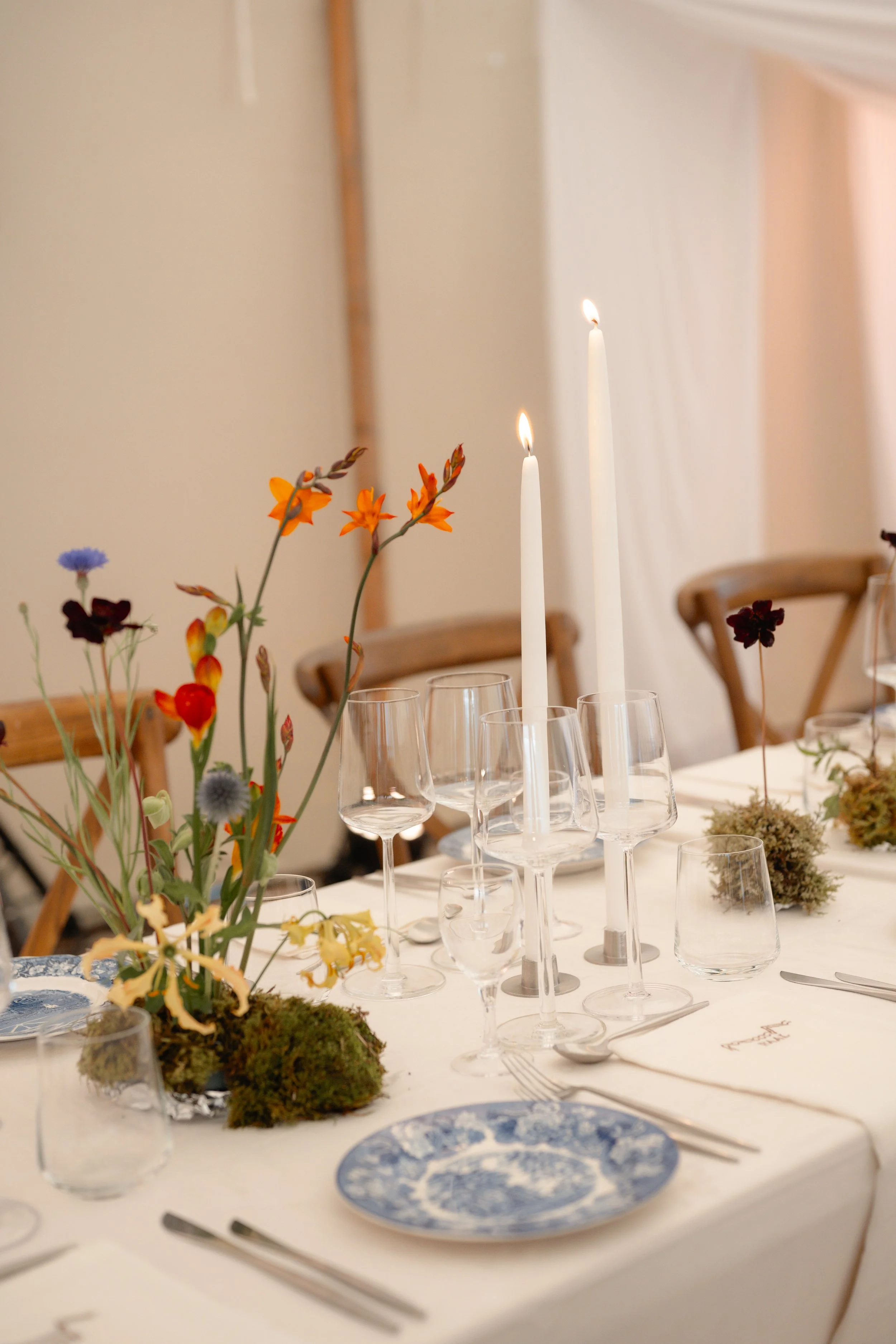 Elegant dining table set with floral centerpiece, candles, wine glasses, and blue and white patterned plates.