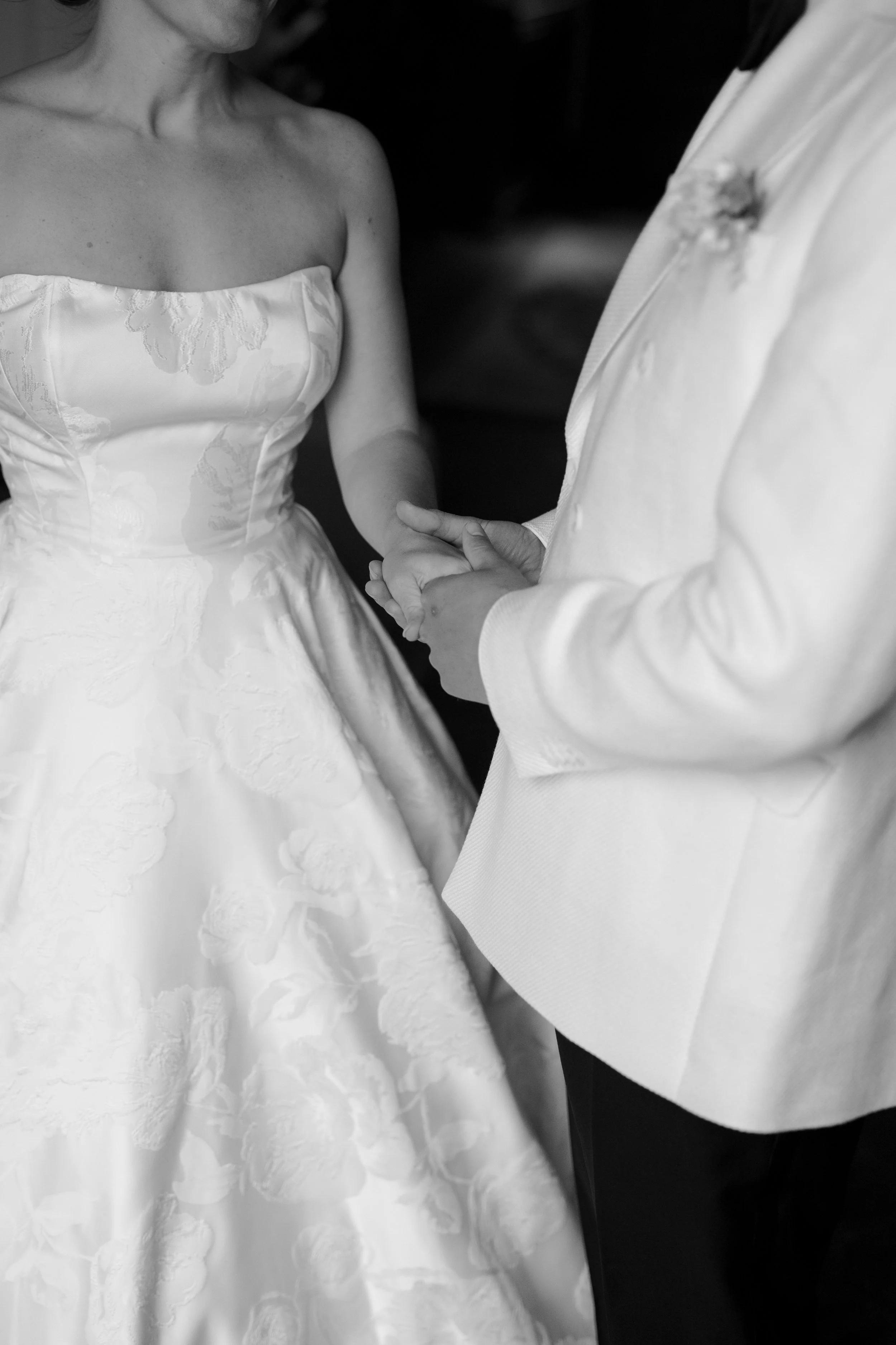 A bride and groom holding hands during their wedding ceremony, in black and white.