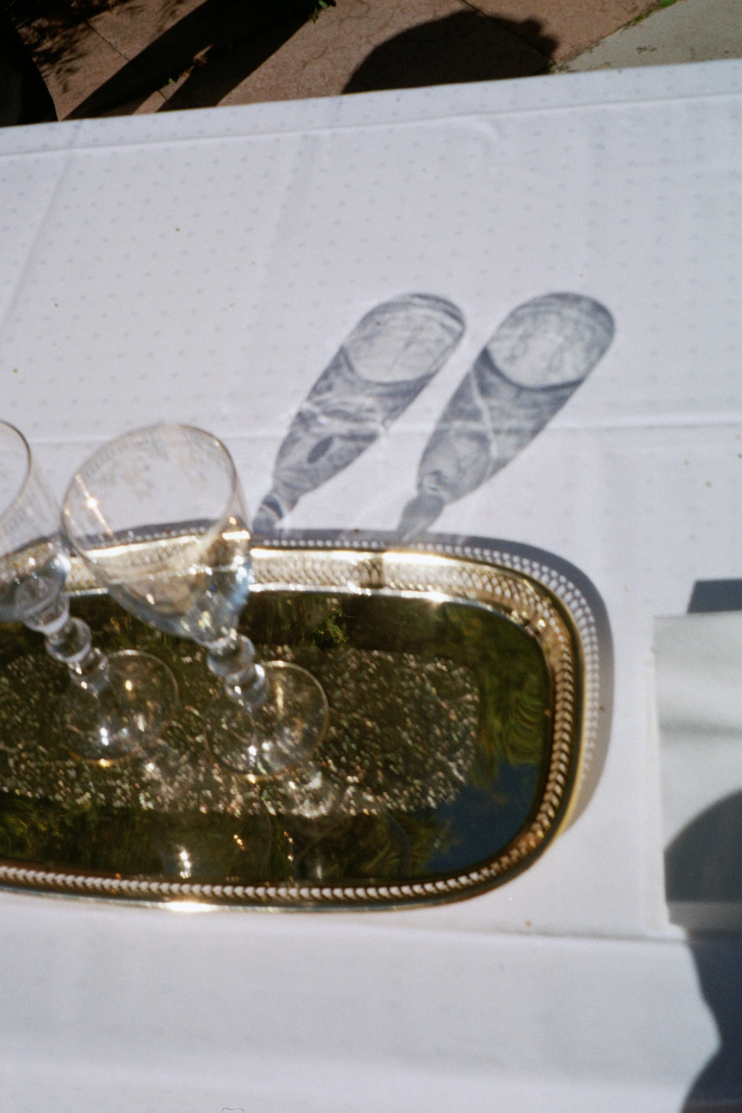 Three empty wine glasses on a white table with sun casting shadows, including a shadow of two fingers.
