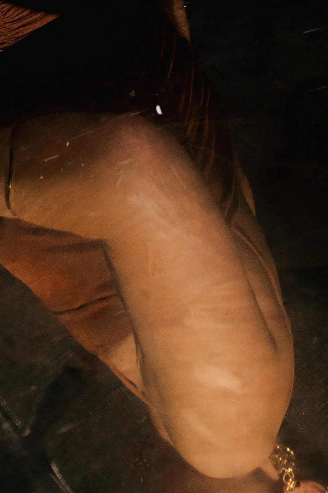 Close-up of a person's thigh with a gold chain bracelet on their ankle, photographed from a side angle.