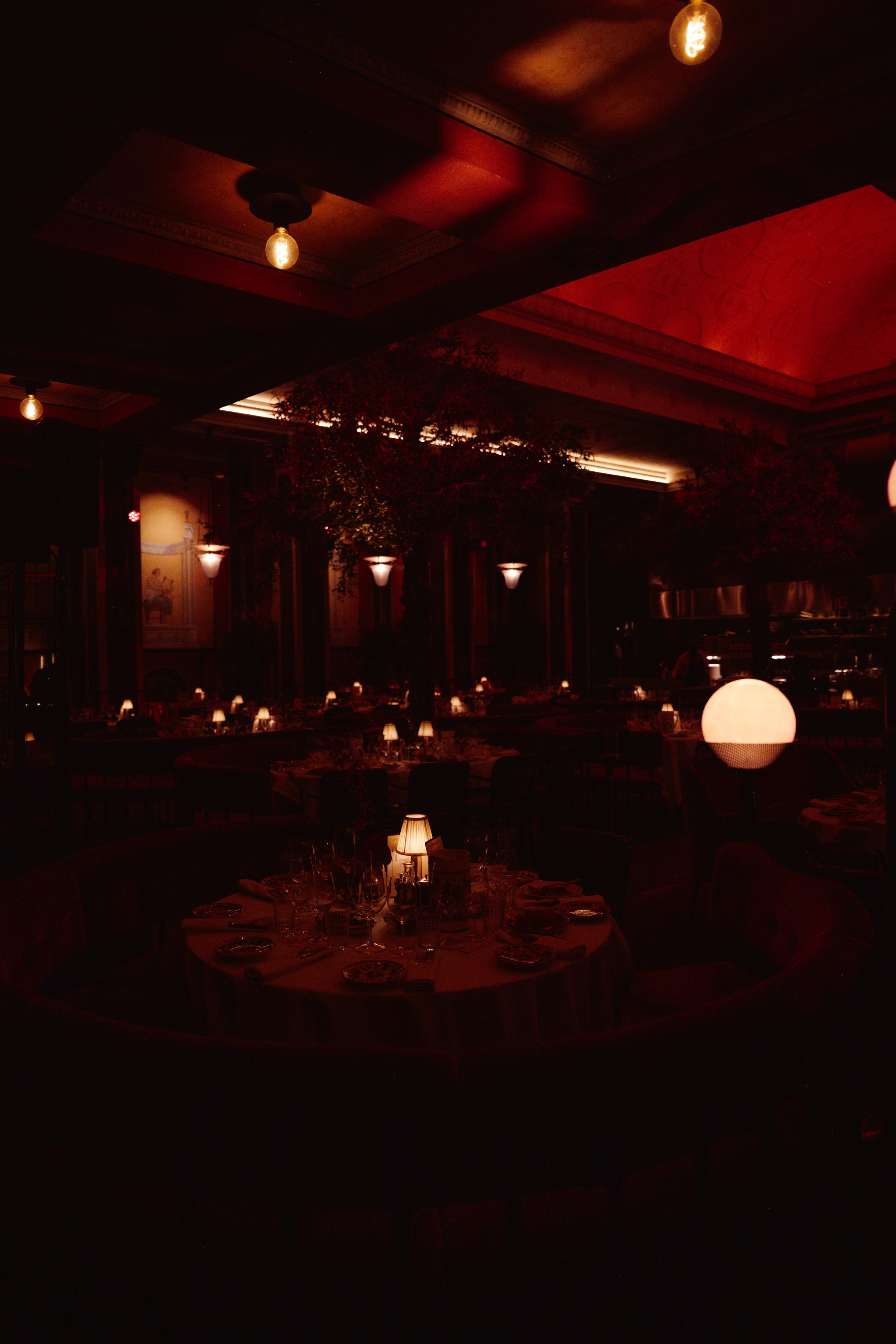 Dimly lit restaurant dining area with round tables, table settings, and warm lighting