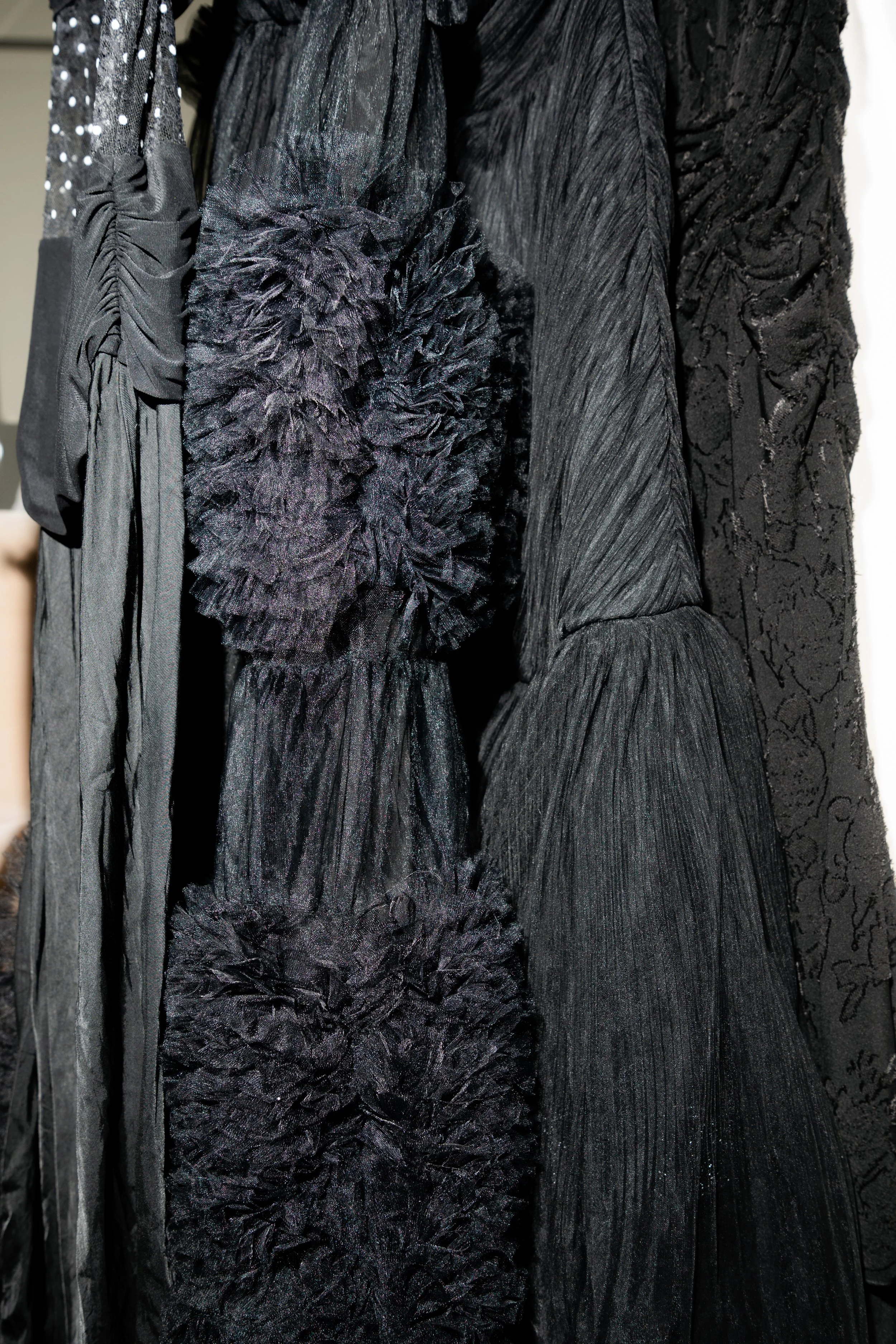 Close-up of black textured dresses with layered ruffles and floral patterns hanging on a rack.