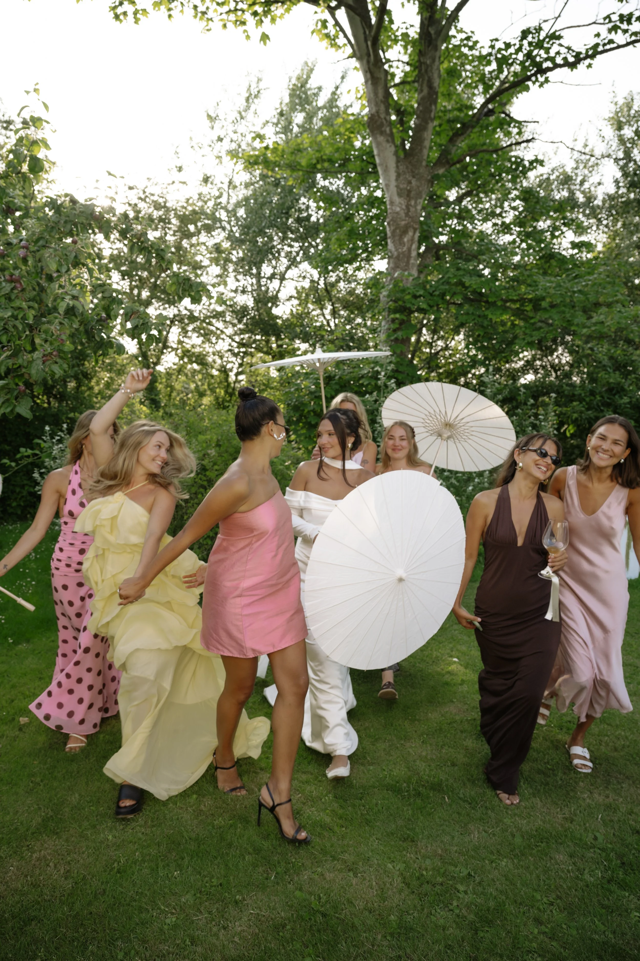 A group of women wearing colorful dresses and holding parasols enjoying an outdoor gathering in a lush, green park.