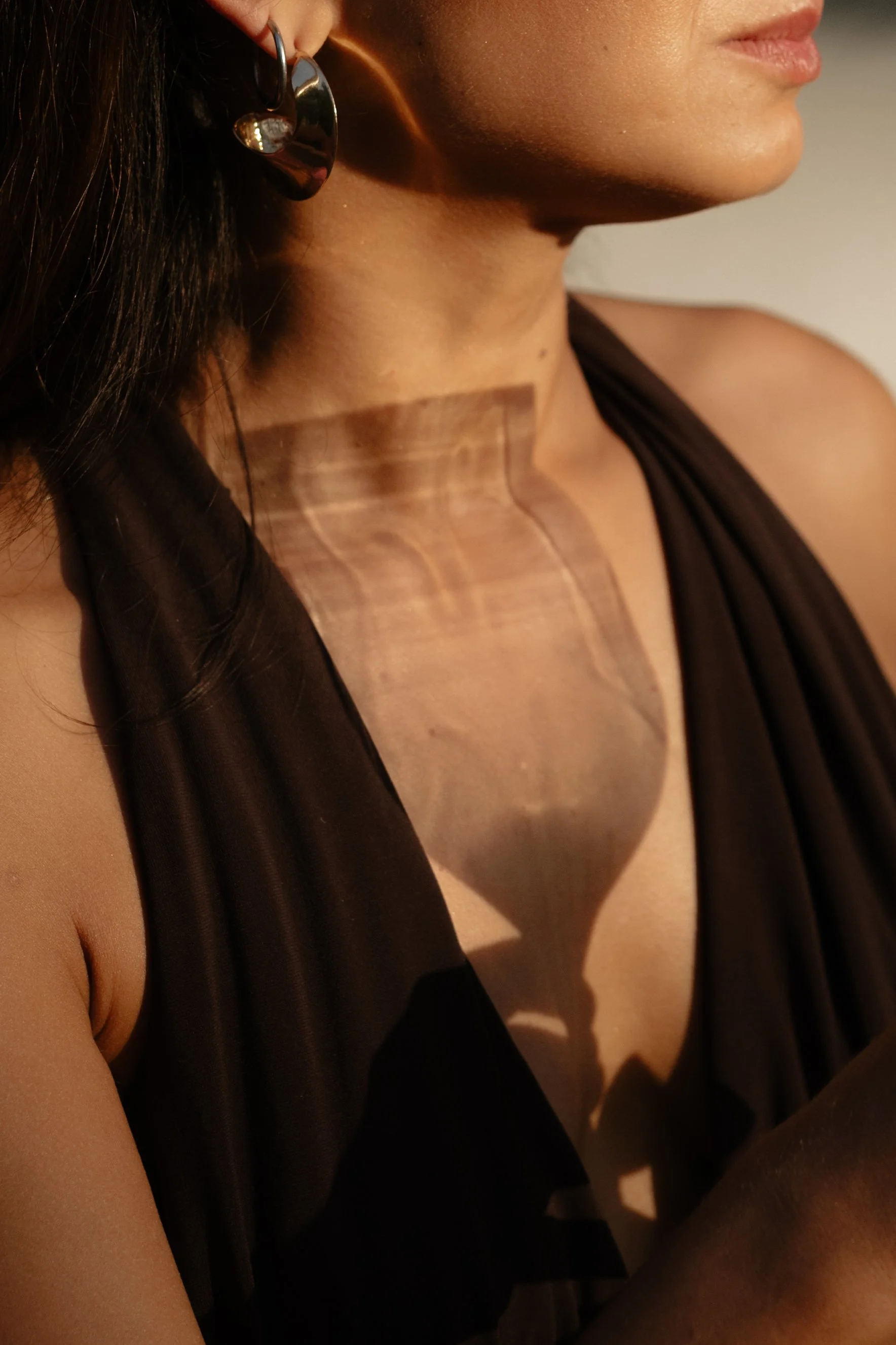 Close-up of a woman's neck and shoulder, showing a wooden shadow box necklace hanging on her neck, with a partly visible face and dark clothing.
