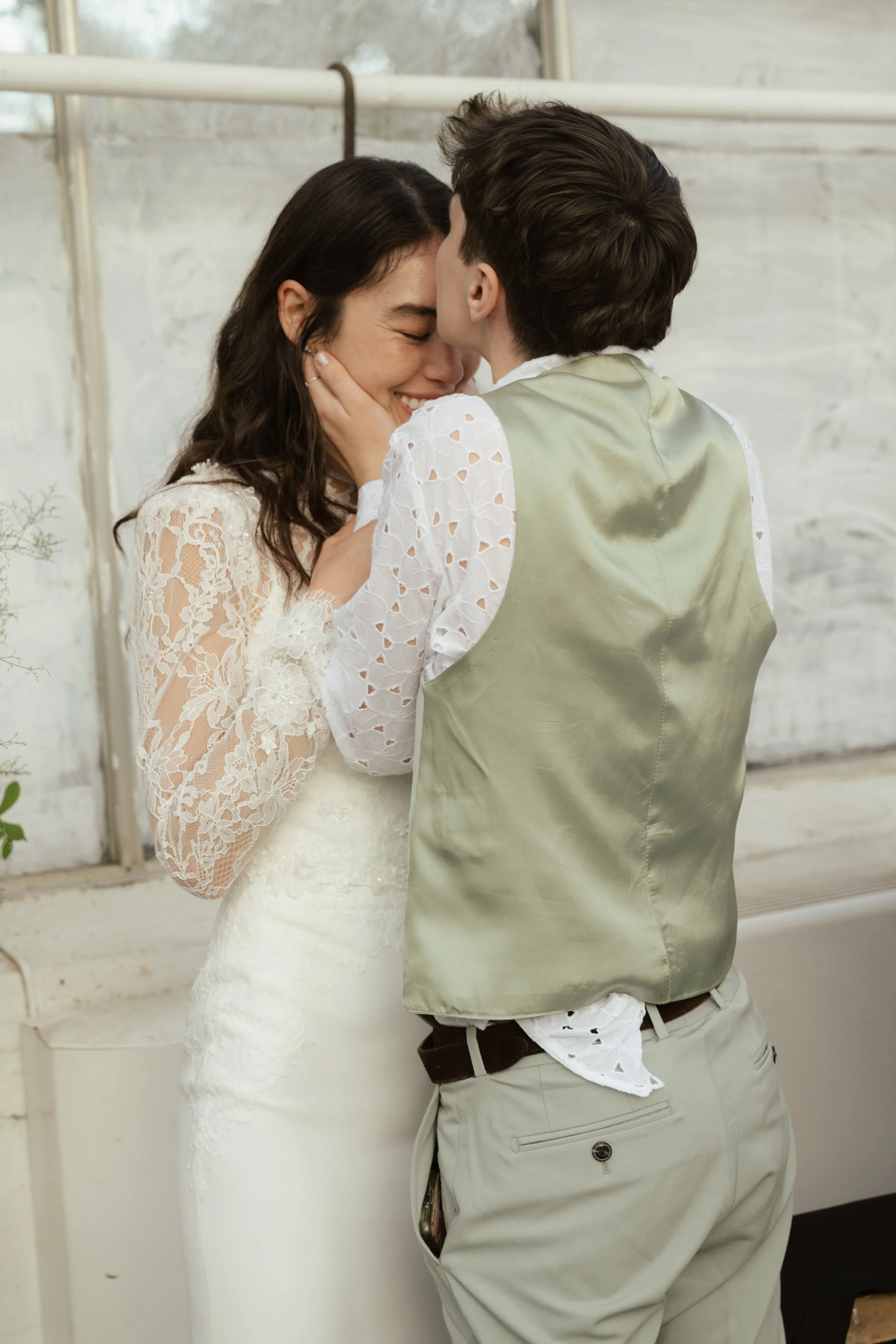 A couple sharing a kiss, with the woman smiling and holding the man's face, in a rustic indoor setting.