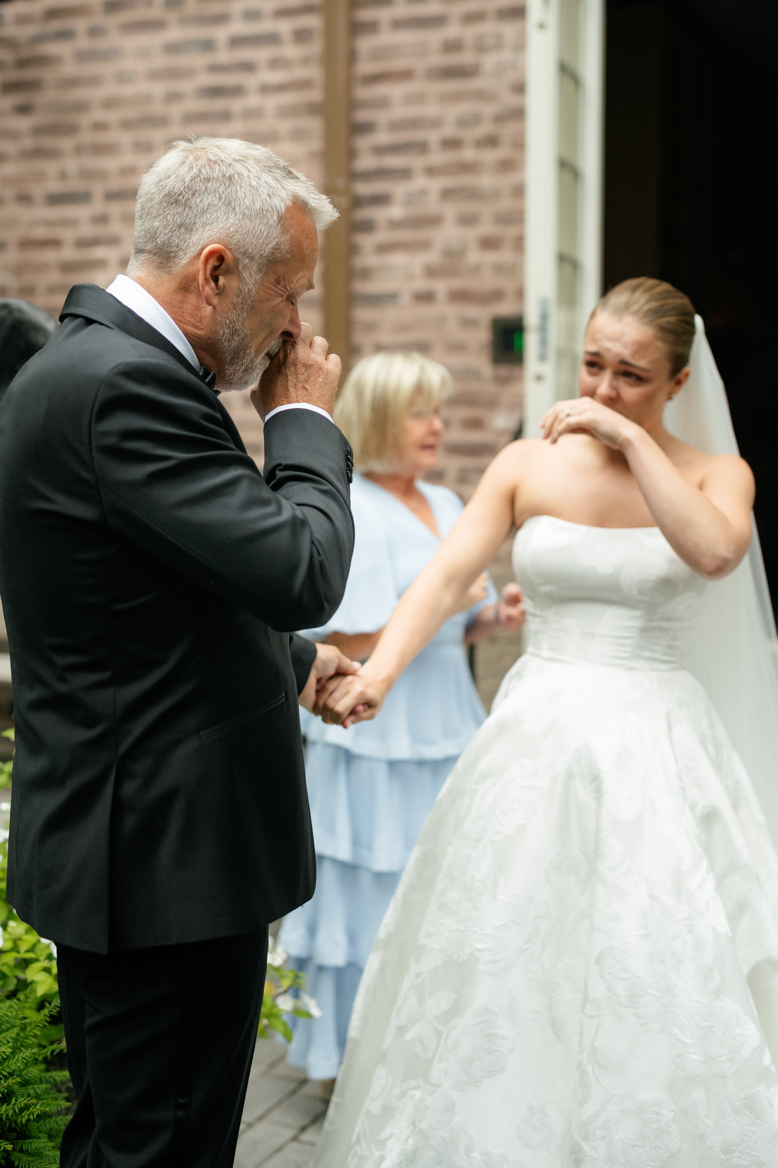 An emotional bride crying as her father, dressed in a black tuxedo, tears up during her wedding ceremony.