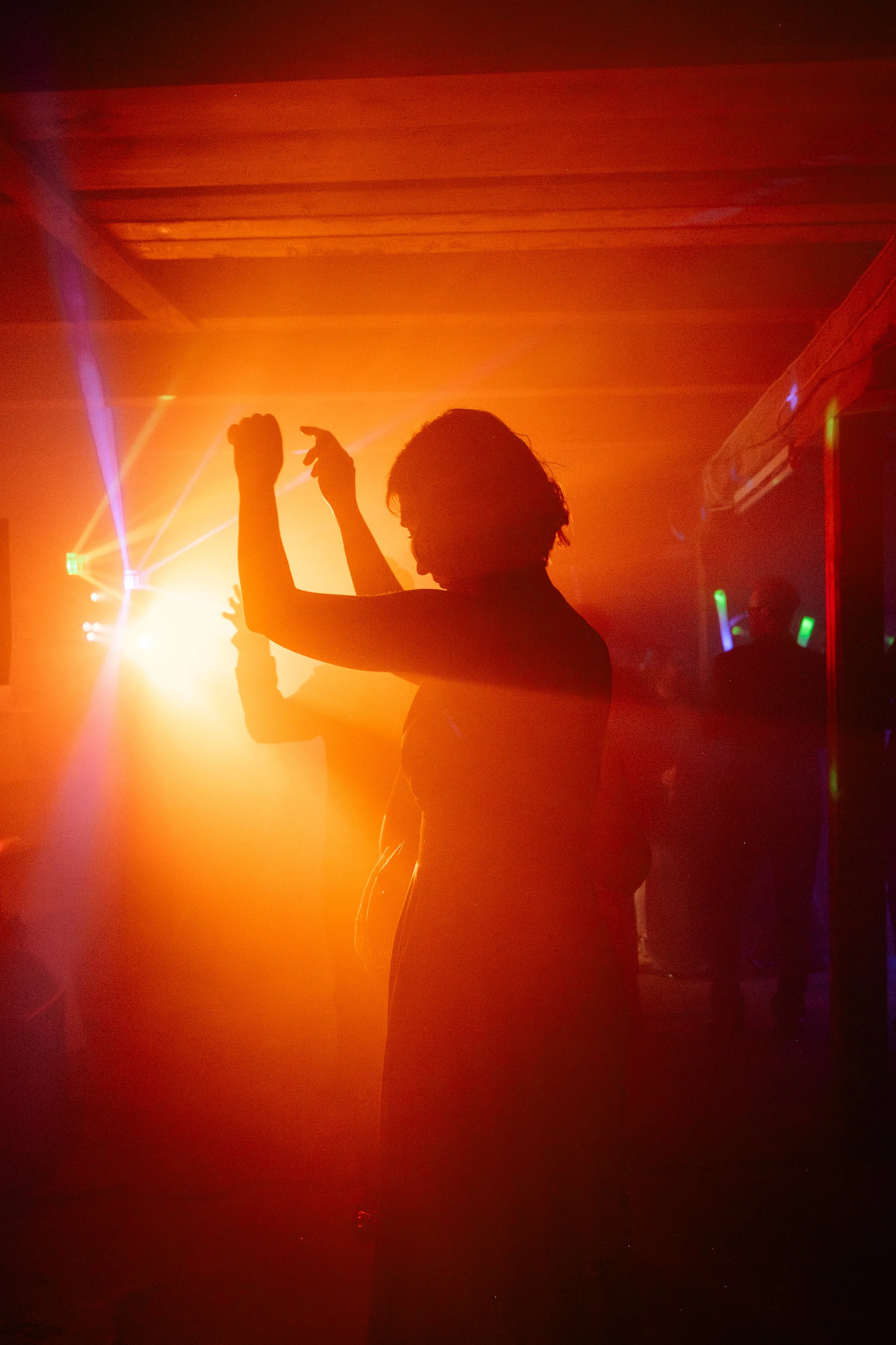 Silhouette of a woman dancing at a party with colorful lights and fog.